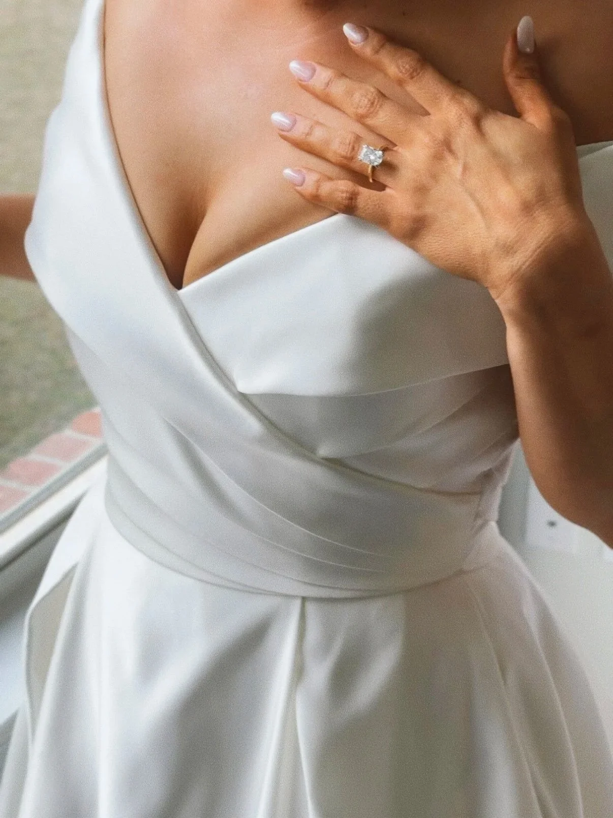 A woman wearing a white dress with her hand on her chest, showing a large engagement ring with a square-cut diamond. Wedding Content Creator, Louisiana Wedding Content Creator, New Orleans Wedding Content Creator, Baton Rouge wedding Content Creator