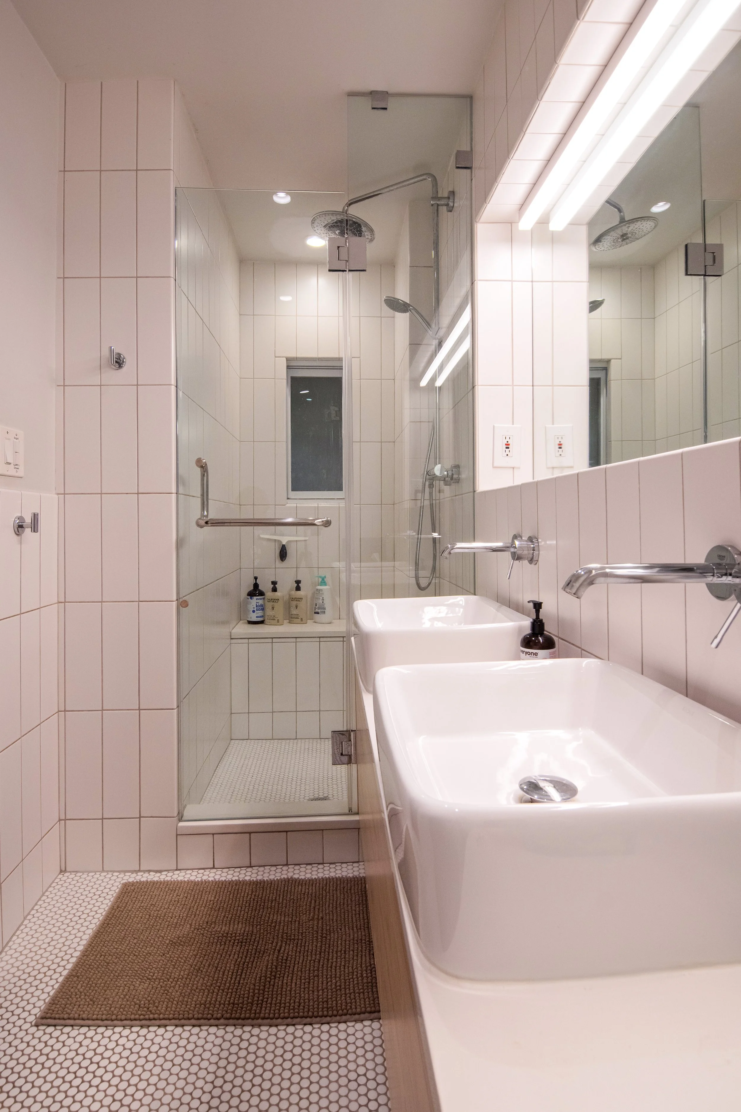 A modern bathroom with a shower area, double sinks, a large mirror, and a window in the shower.