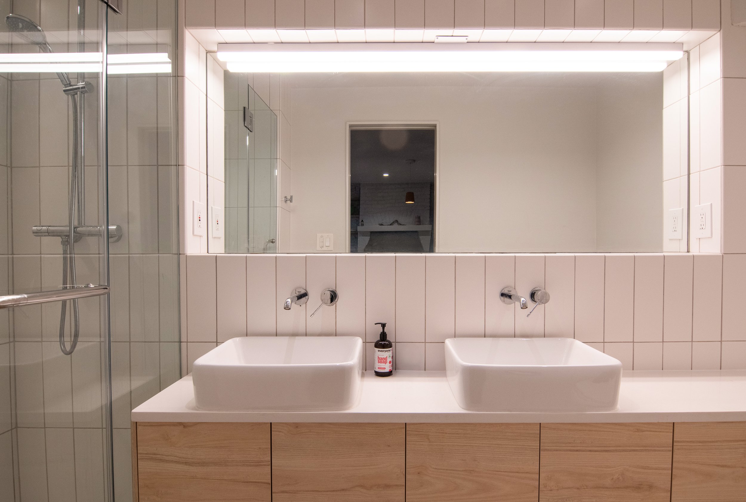 Modern bathroom with double square vessel sinks, wooden vanity, large mirror, and walk-in shower with glass enclosure.