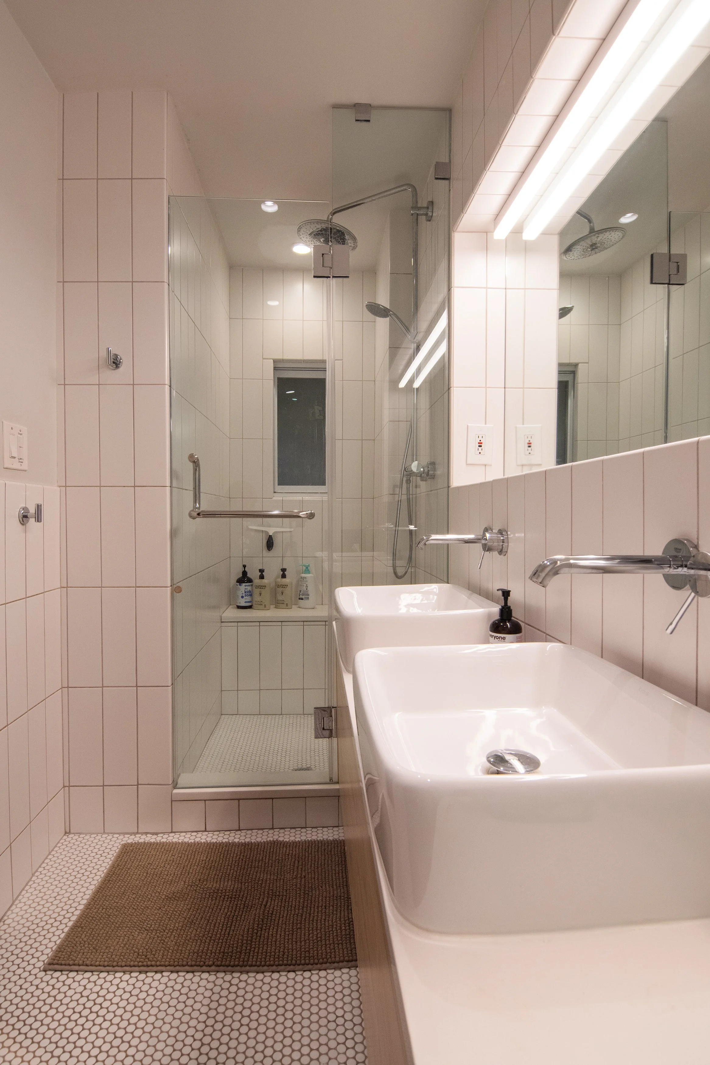 A modern bathroom with a shower area, double sinks, a large mirror, and a window in the shower.