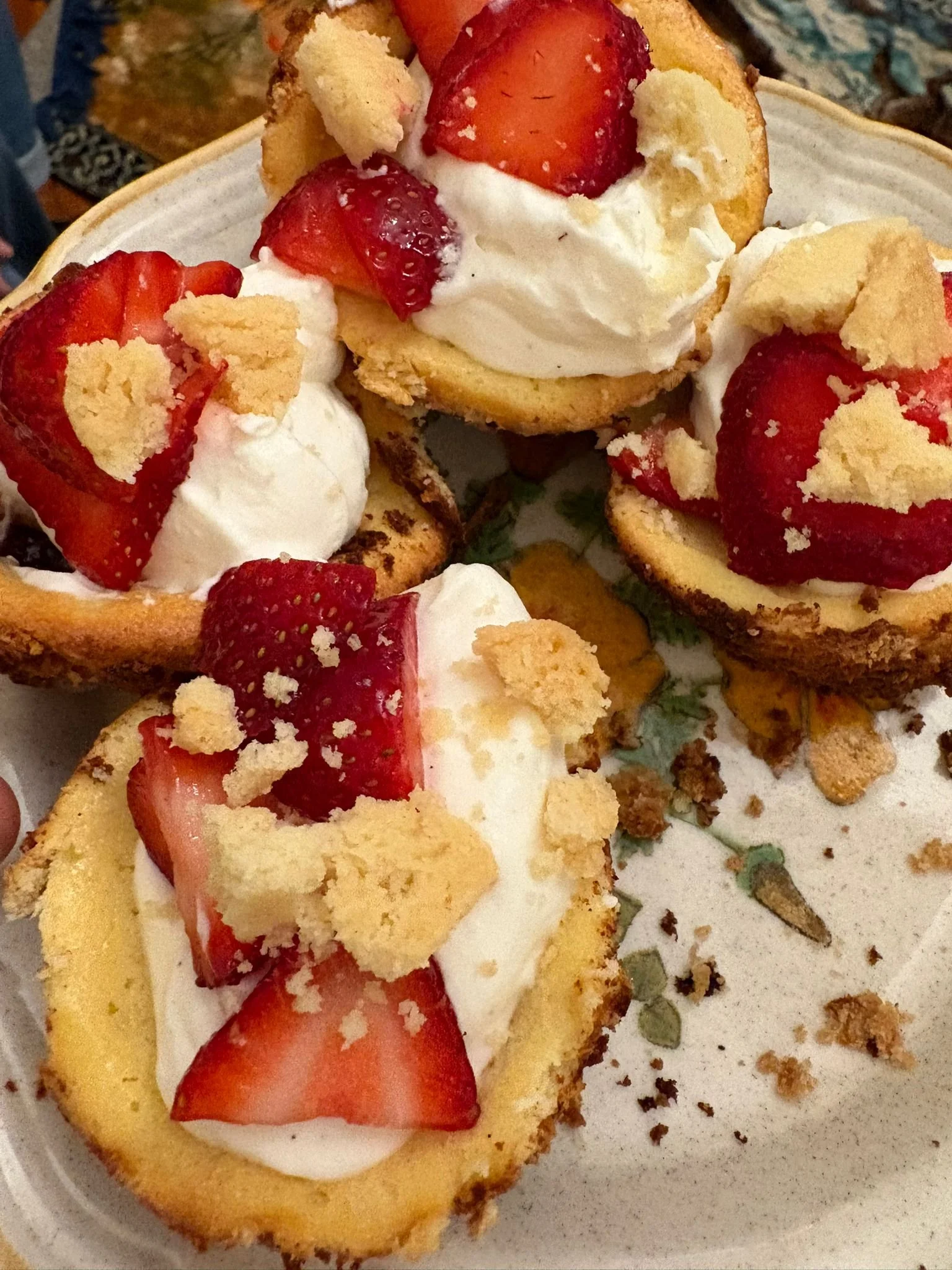 Mini shortcakes topped with strawberries, whipped cream, and crumbled cookies on a decorative plate.