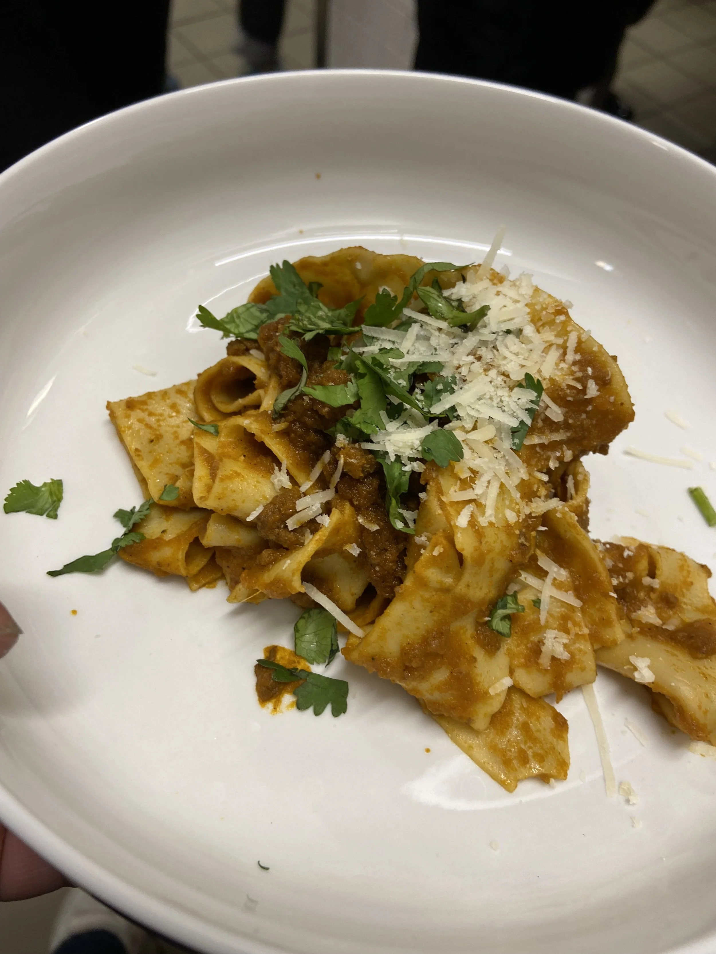 Close-up of a plate of pasta with a meat sauce, topped with grated cheese and garnished with fresh herbs.