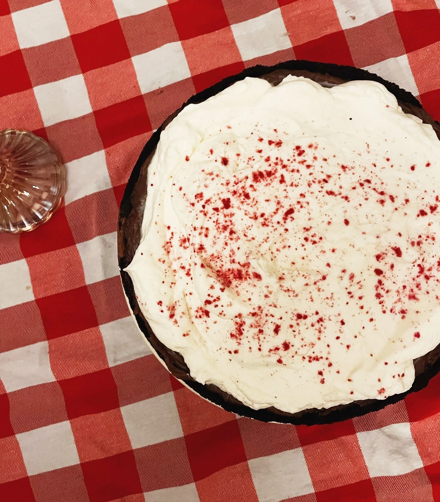 Dessert with white frosting sprinkled with red crumbs, served on a checkered red and white tablecloth.