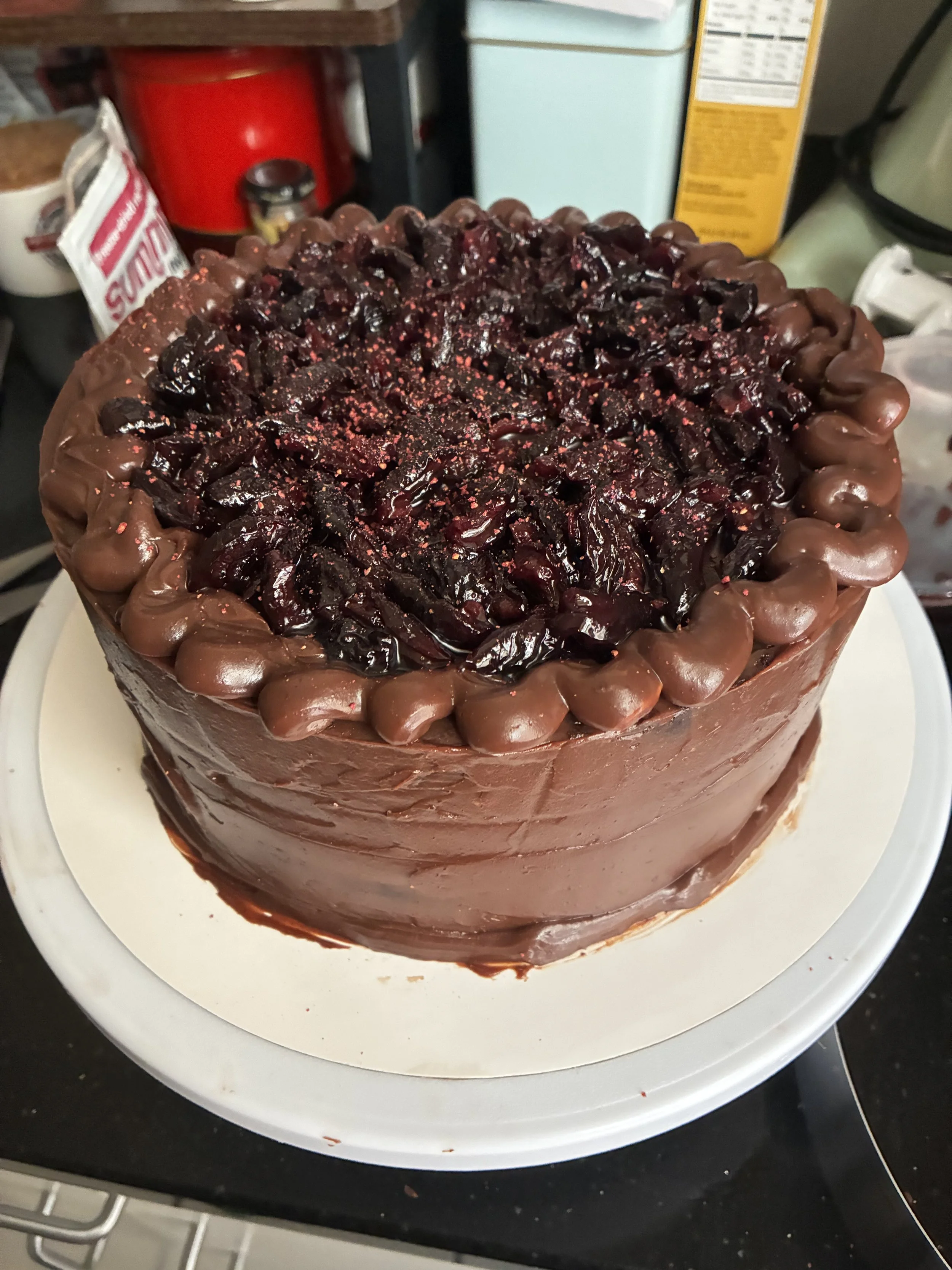 Chocolate cake topped with cherry pie filling and sprinkled with red sugar crystals, decorated with chocolate frosting around the edges.