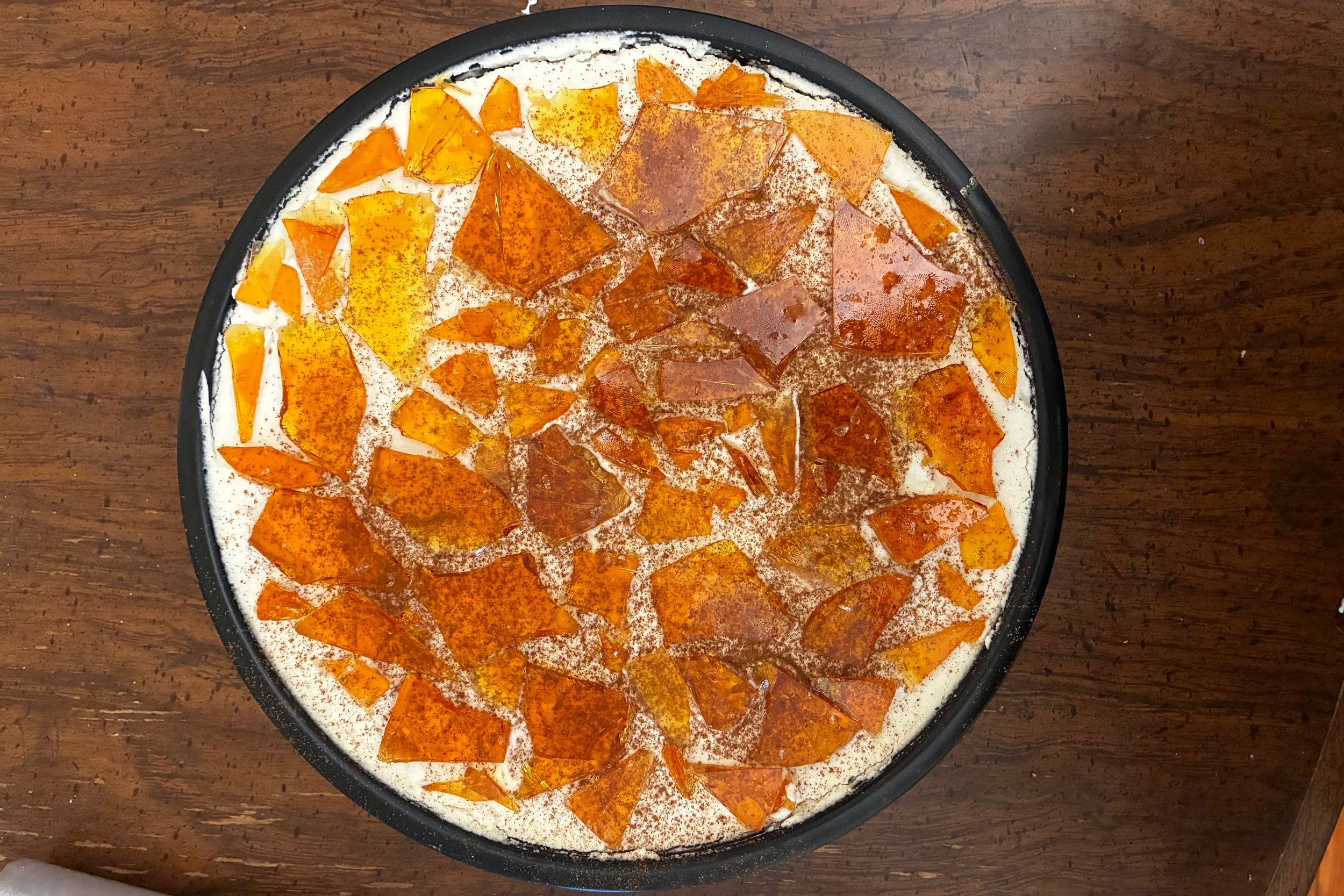A circular dish filled with a mixture of orange, yellow, and clear broken glass pieces on a wooden surface.