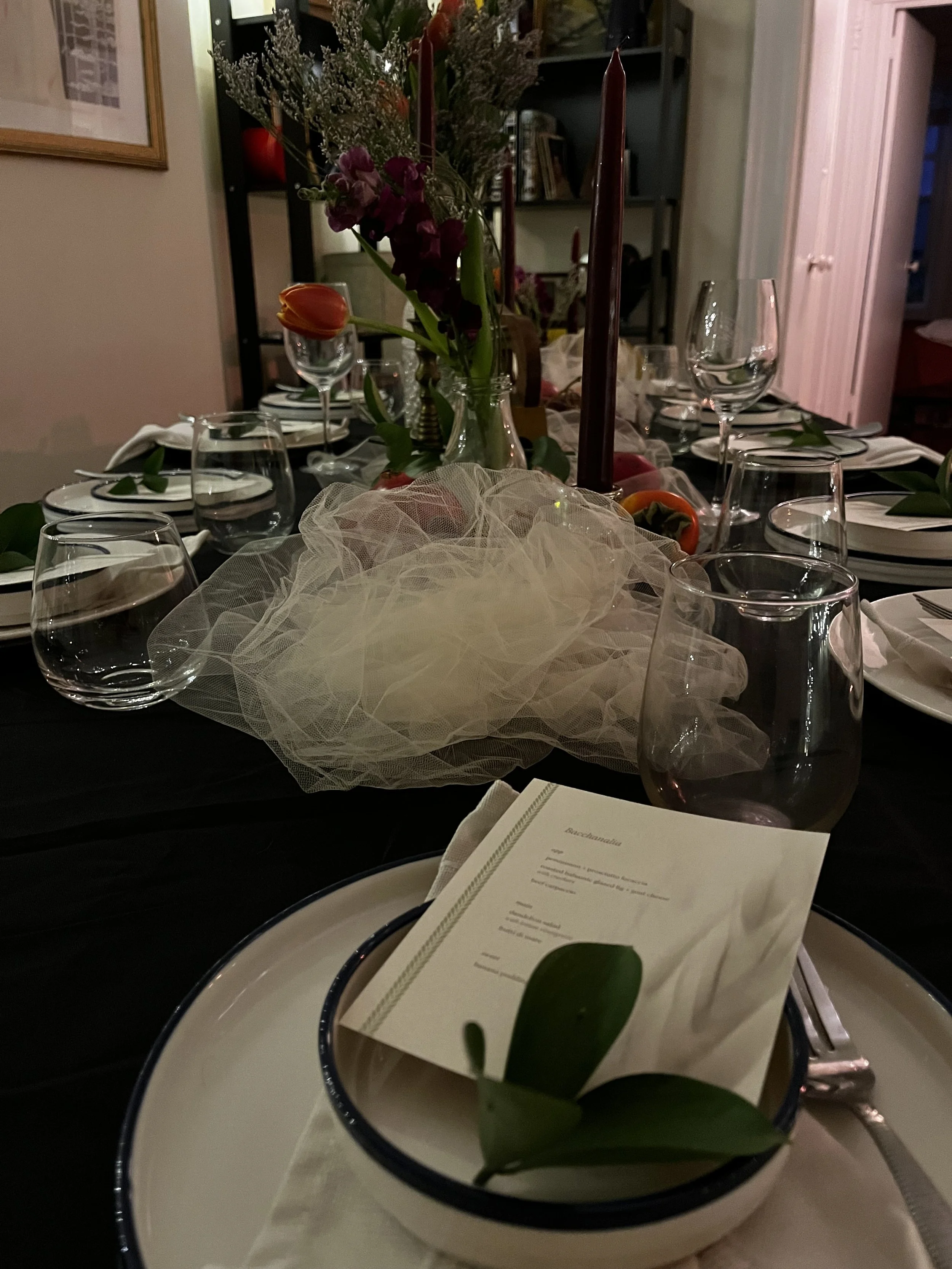 A formal dining table set with wine glasses, plates, utensils, and a menu card, decorated with flowers and candles.
