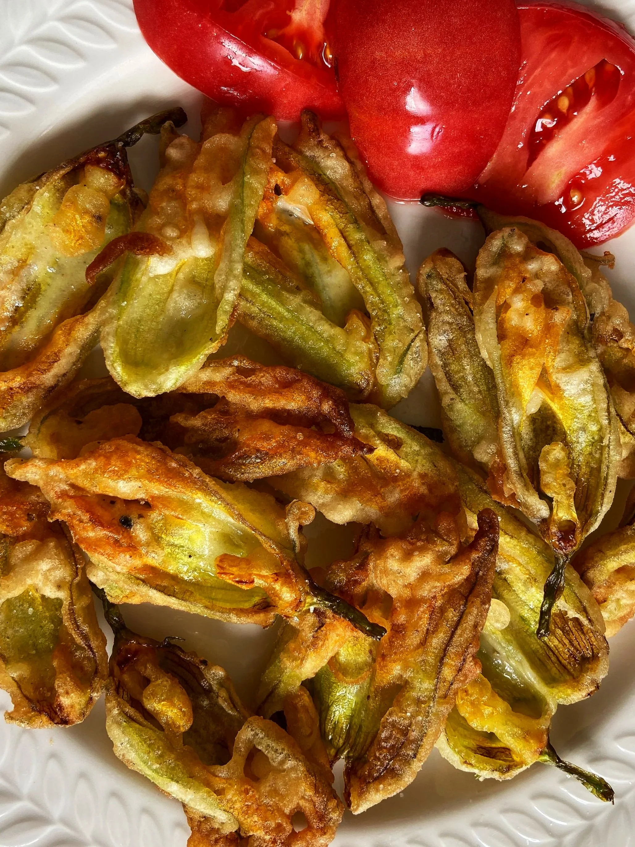 Close-up of assorted tempura vegetables, including slices of zucchini, bell pepper, and eggplant, served on a white plate.