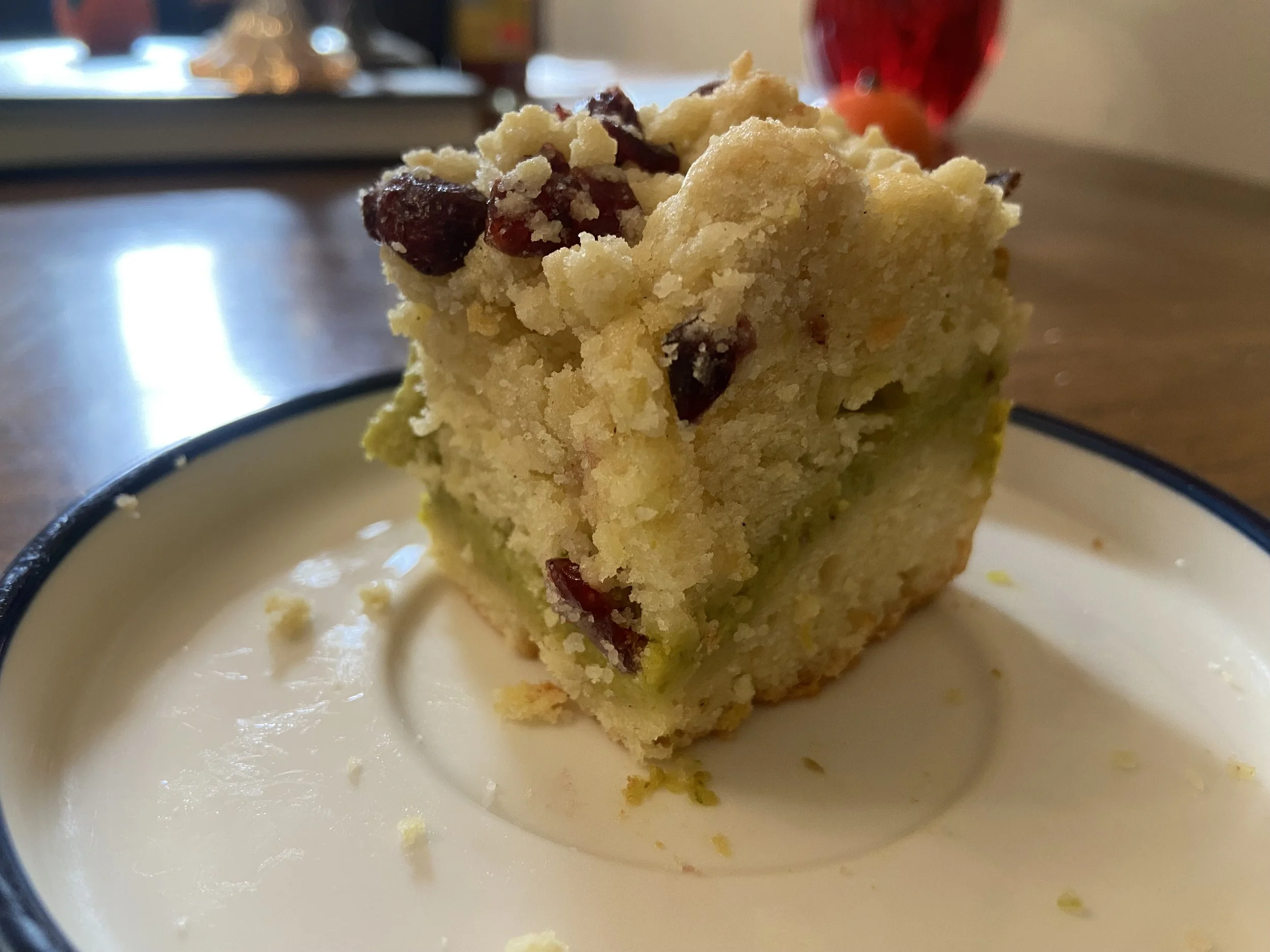 A square piece of cake with fruit pieces on top, served on a white plate with a dark rim.