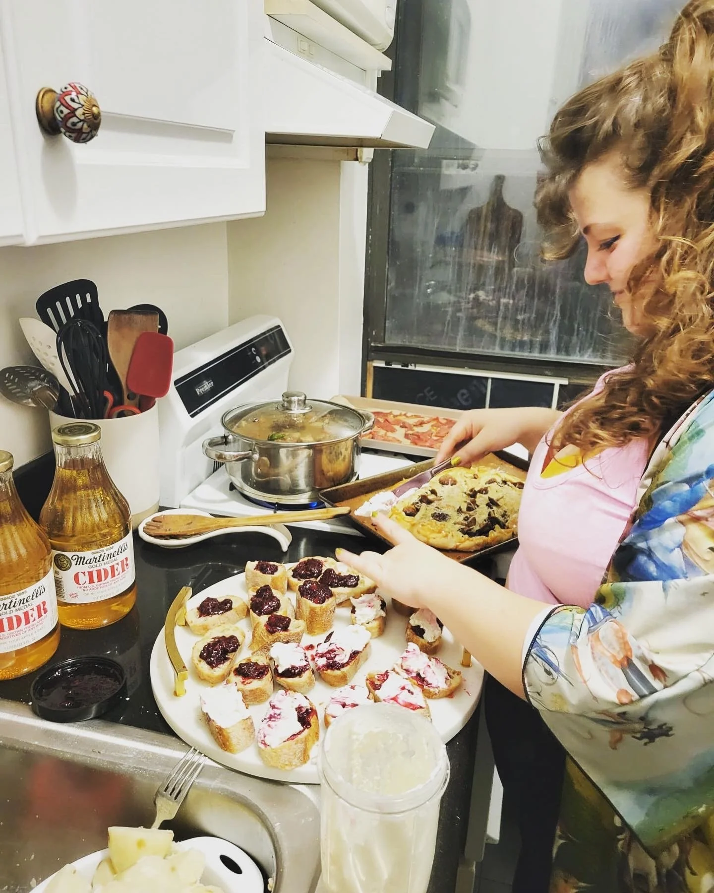 A woman preparing small desserts on a kitchen counter, with a tray of cookies, jars of honey, and various kitchen utensils.
