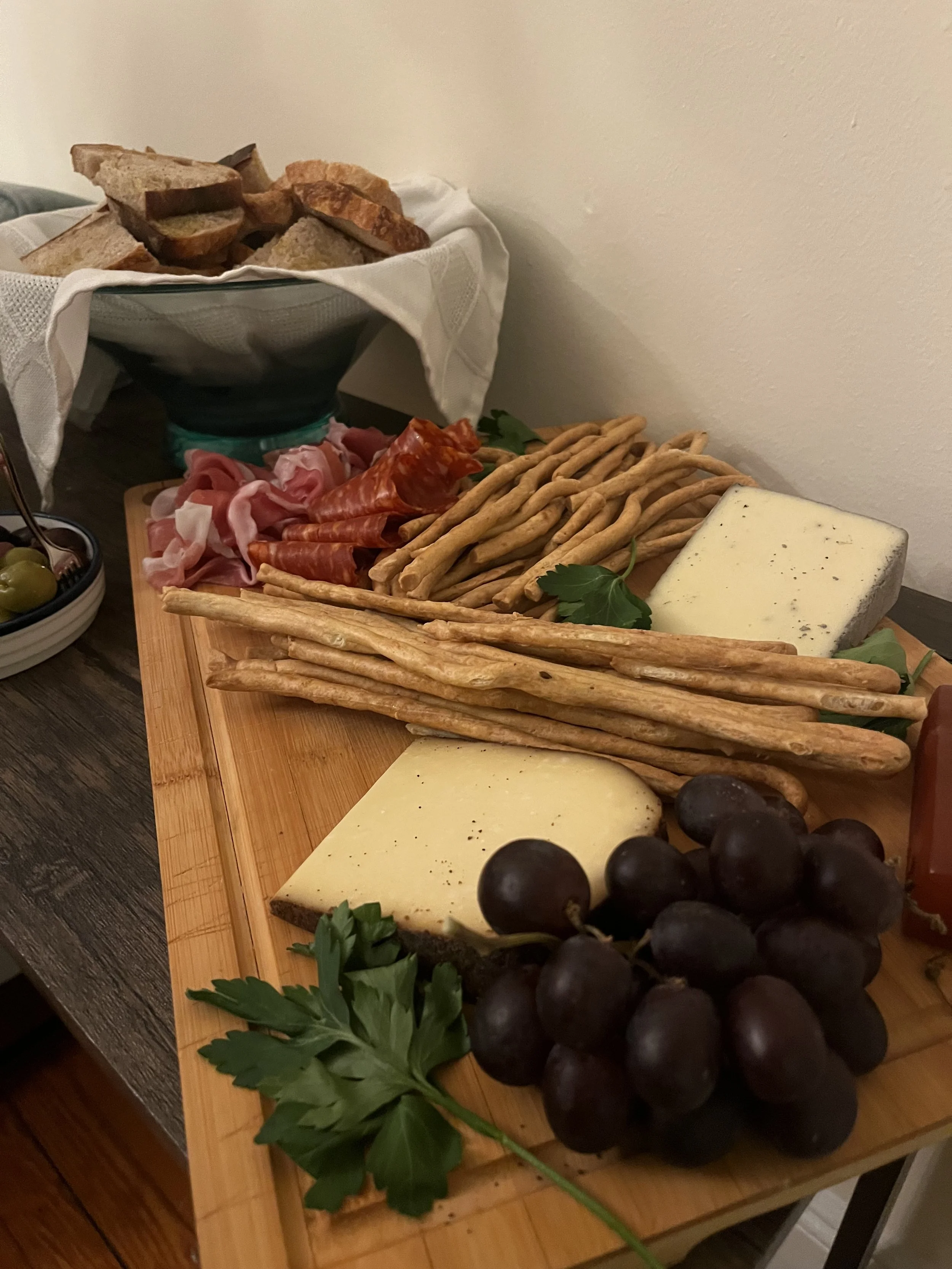 Charcuterie board with cheese, grapes, bread, and cured meats, on a wooden surface with a cheese ball in the background