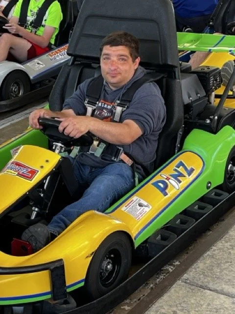 Michael sitting in a green and yellow go-kart, smiling, at an indoor entertainment venue.