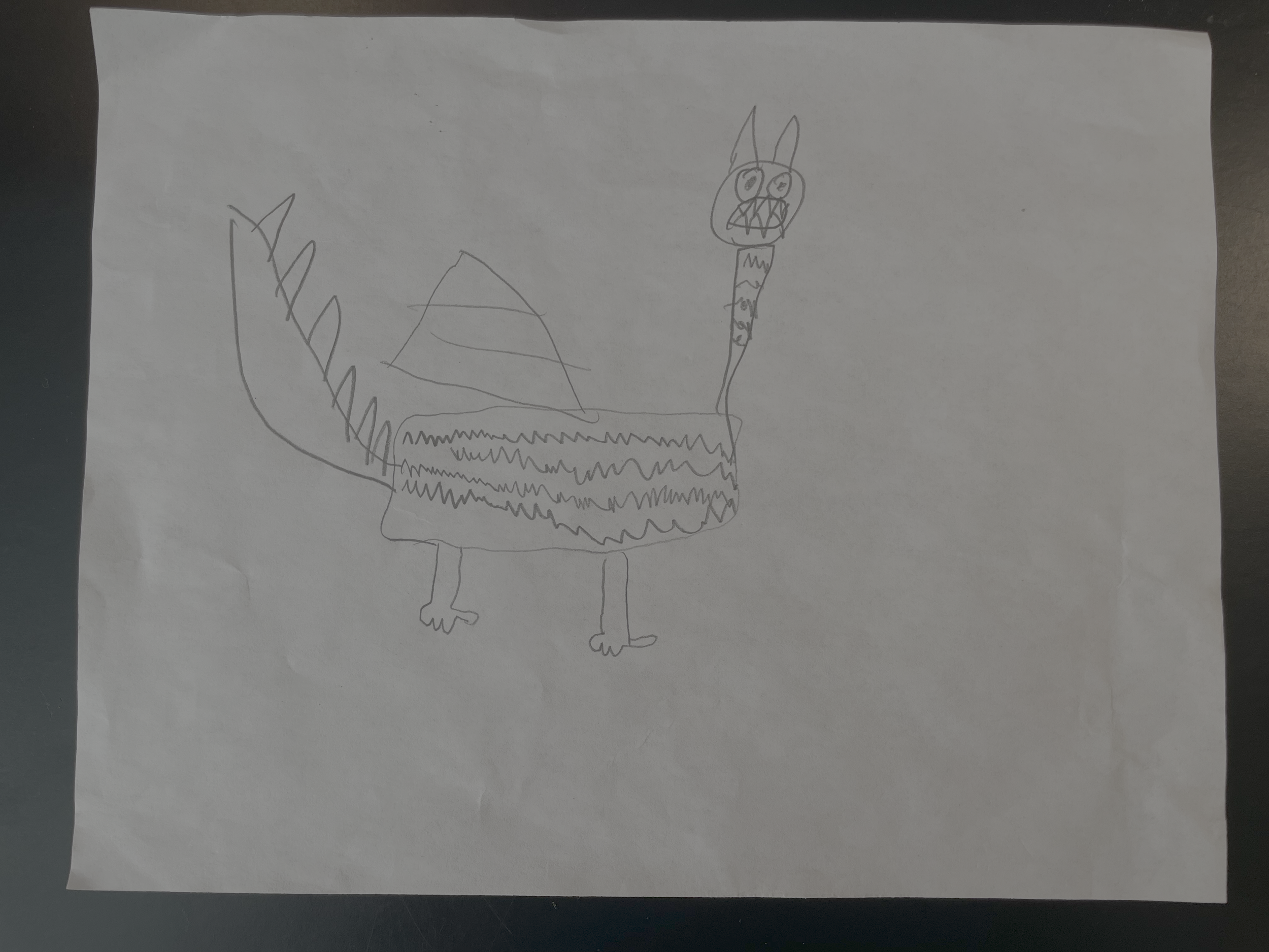 A child's drawing of a dragon with wings, a long neck, and four legs, with a face that has large round eyes and a wide mouth, on white paper.