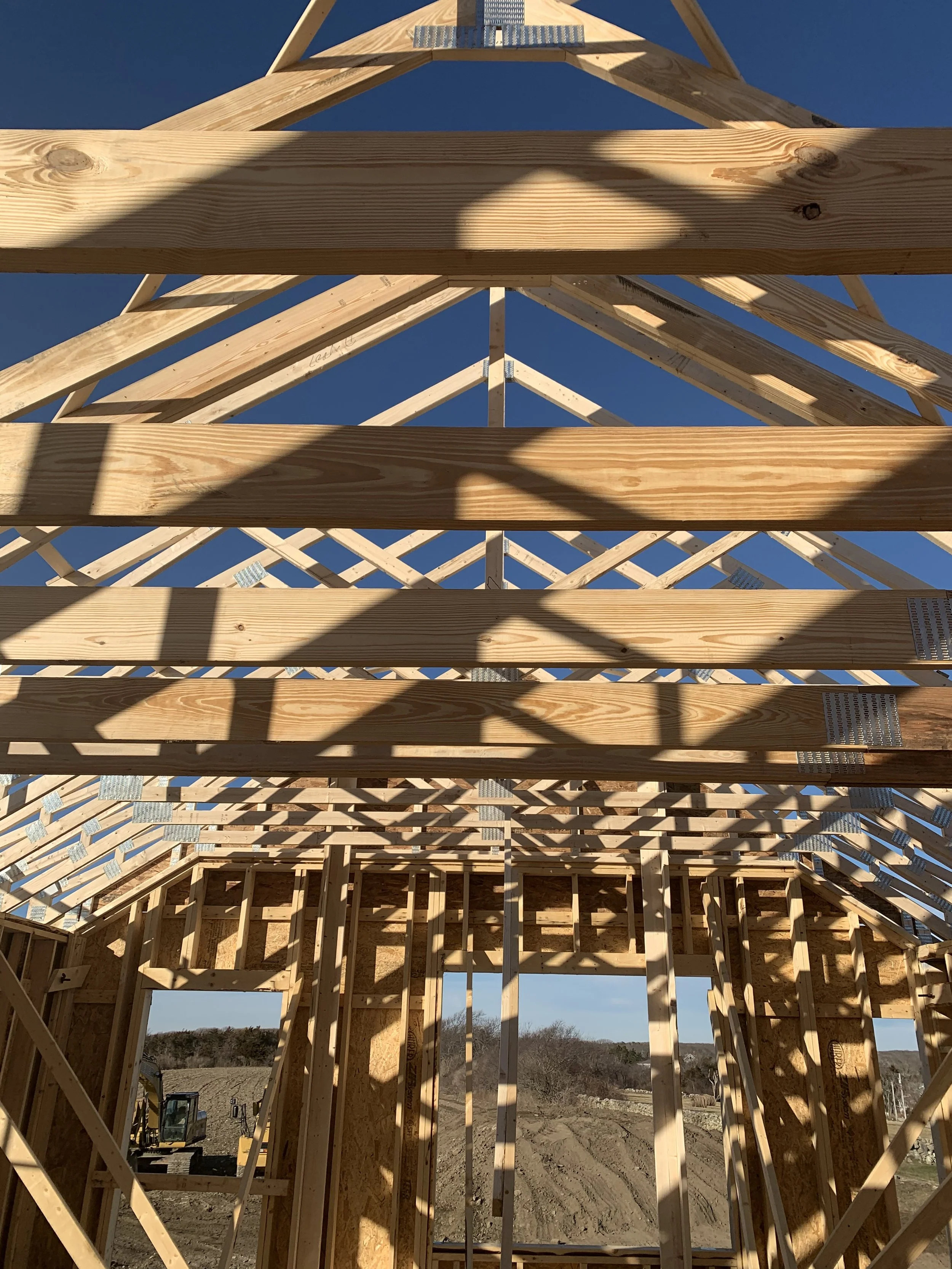 Wooden framework of a building under construction with a clear blue sky in the background.