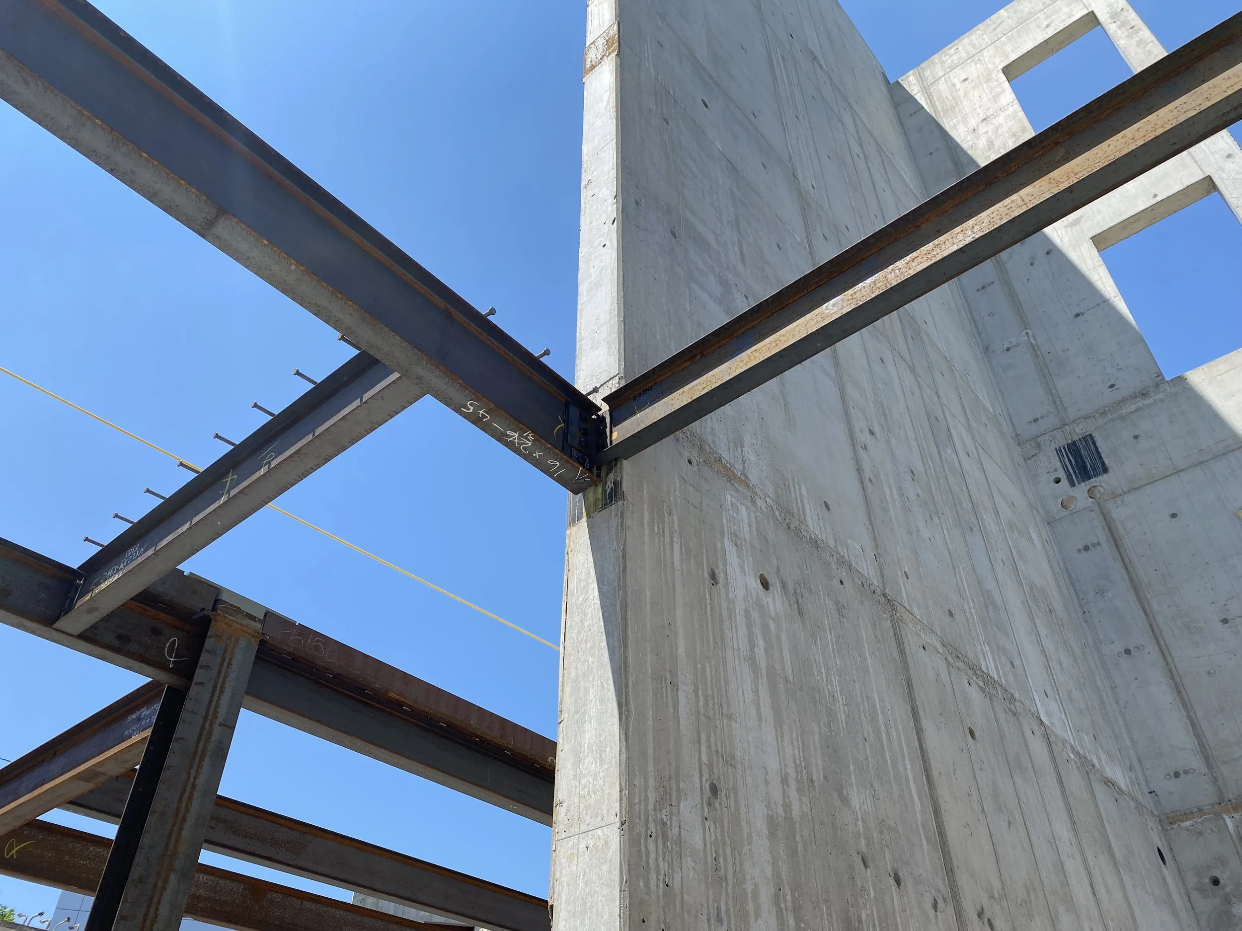 Construction site showing steel beams and concrete wall under a clear blue sky.
