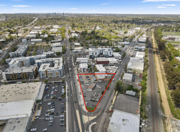 Aerial view of a city area with a triangular plot of land outlined in red, surrounded by roads, buildings, and train tracks.