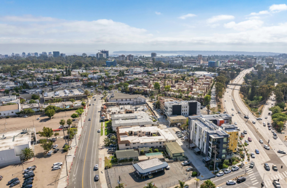 Aerial view of a city with streets, buildings, and highways, with a distant skyline and water in the background.