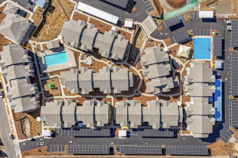 Aerial view of a residential complex with multiple houses, a swimming pool, and sports courts.