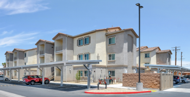 Multi-story apartment complex with covered parking area, cars, and a blue sky.