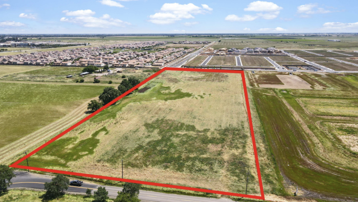 A large undeveloped plot of land outlined in red surrounded by fields, roads, and a residential area in the background.