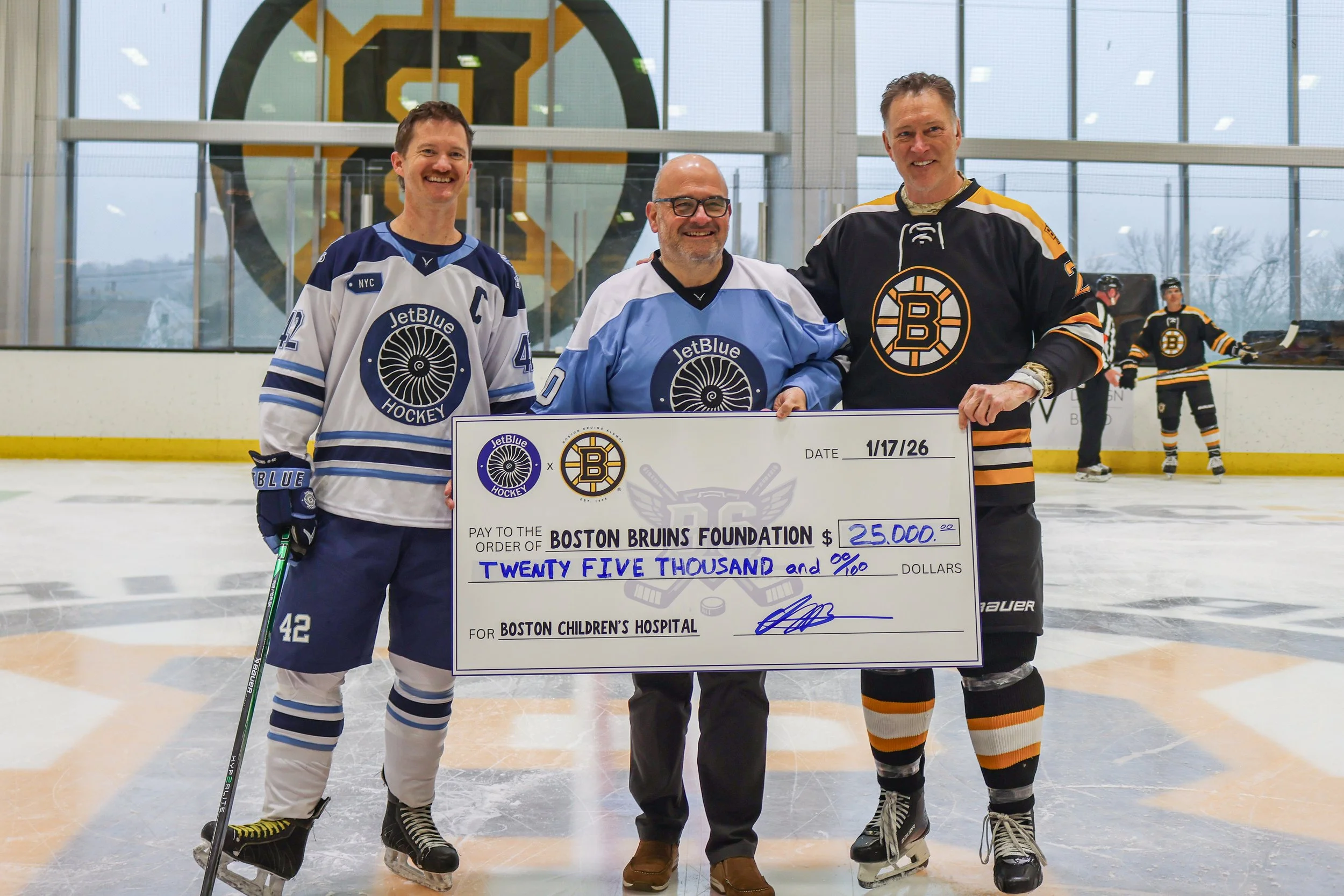 Nolan Collins and JetBlue President: Marty St. George present a check to the Boston Bruinds Foundation to Boston Bruins legend and icon: Bob Sweeney.