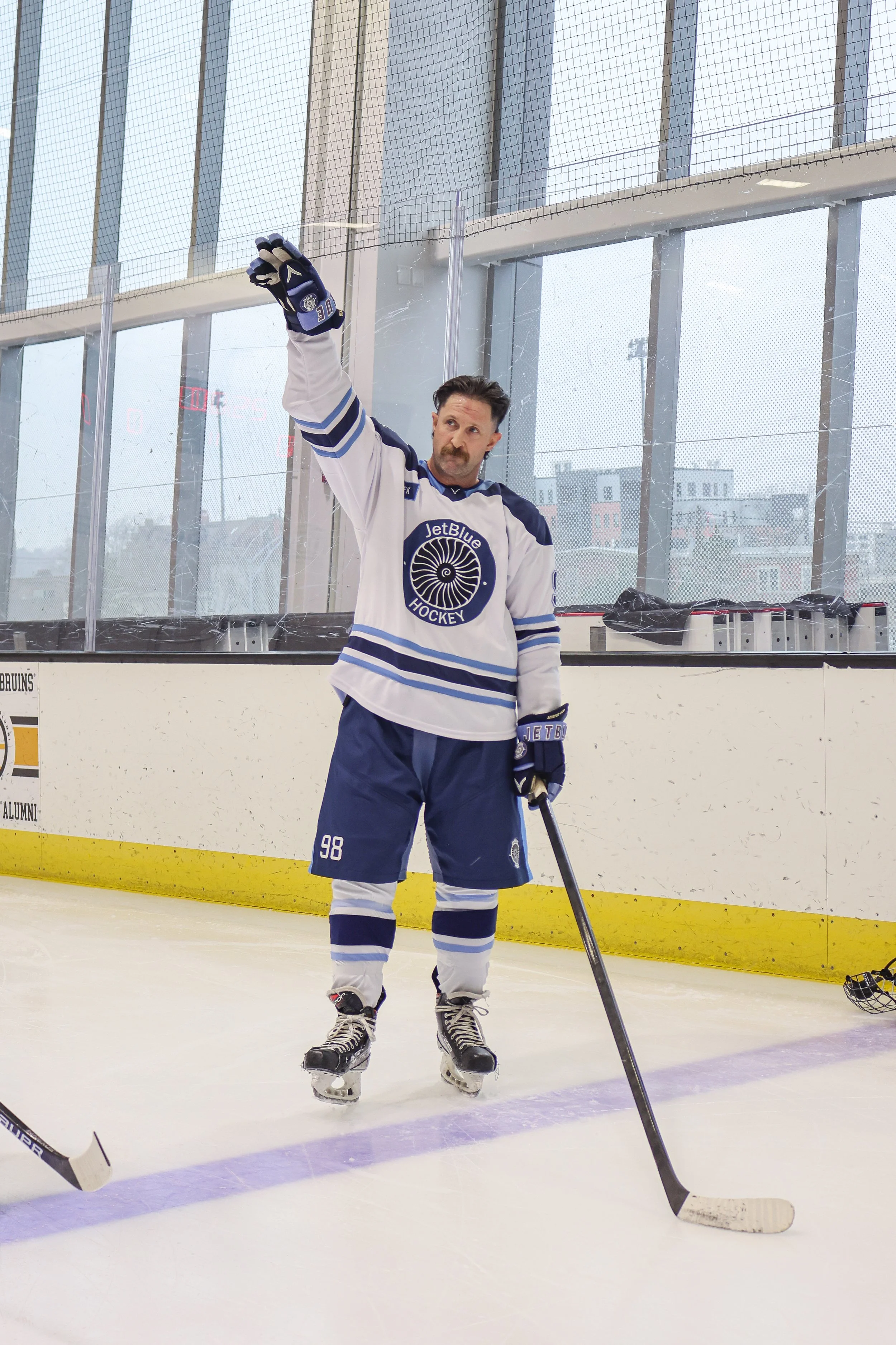 A man in a blue and white hockey uniform on the ice rink raising his glove in the air.