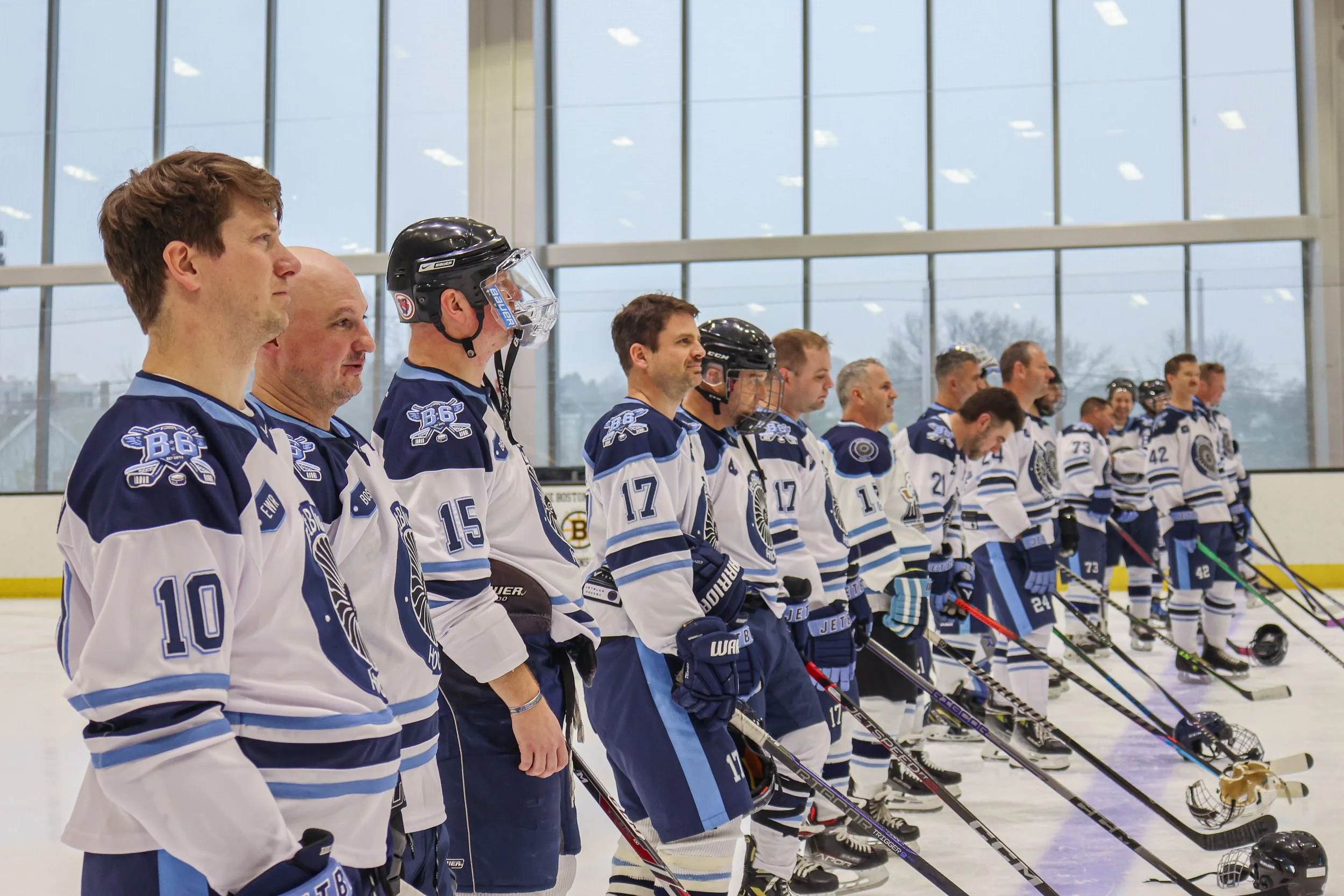 Hockey team lined up on the ice in a rink, wearing matching jerseys, with some players wearing helmets, standing side by side before a game.