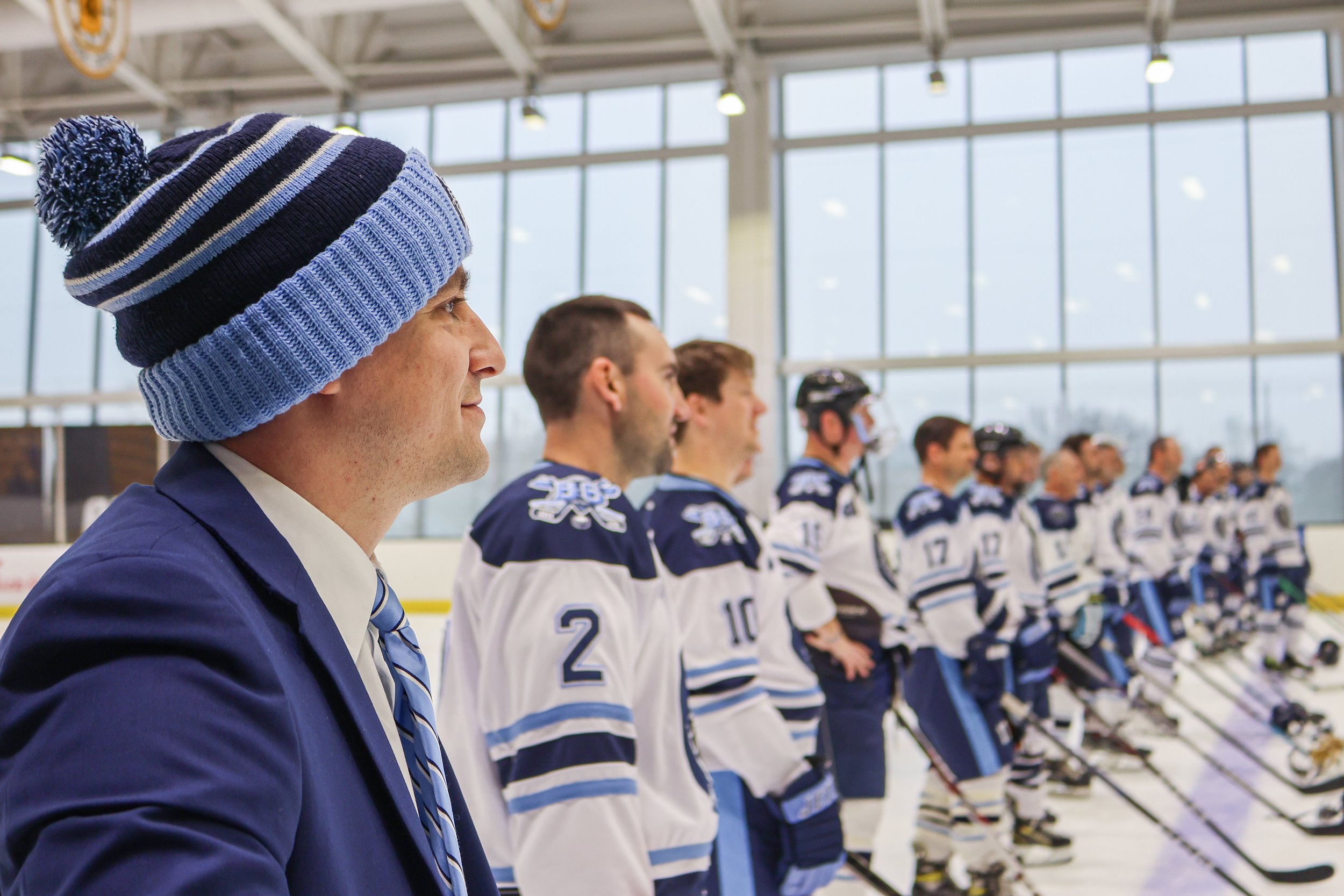 Hockey coach in a suit and knit hat standing with the team in an ice rink.