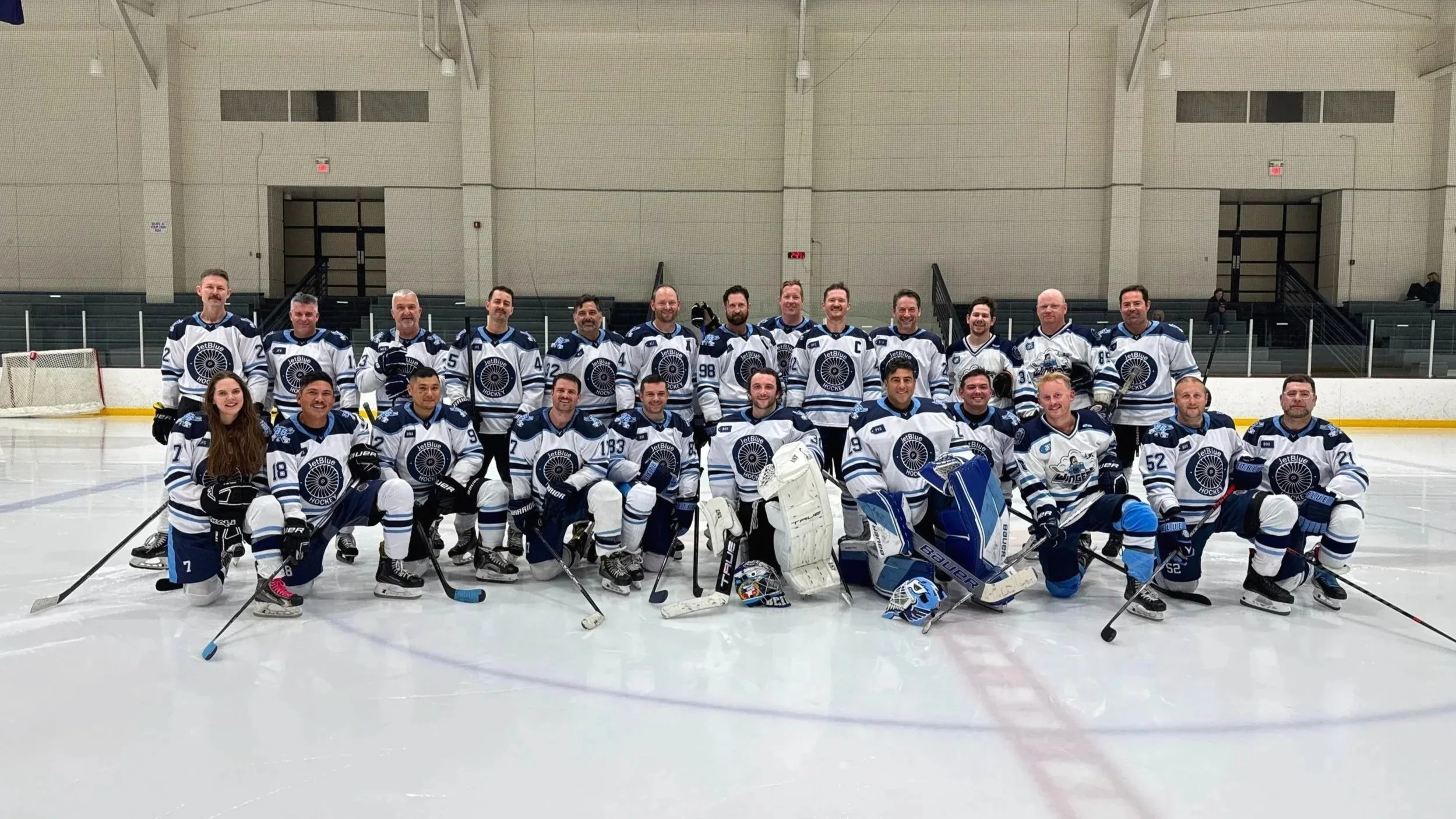 A team of hockey players and a few staff members posing on an ice rink in their hockey gear and jerseys.