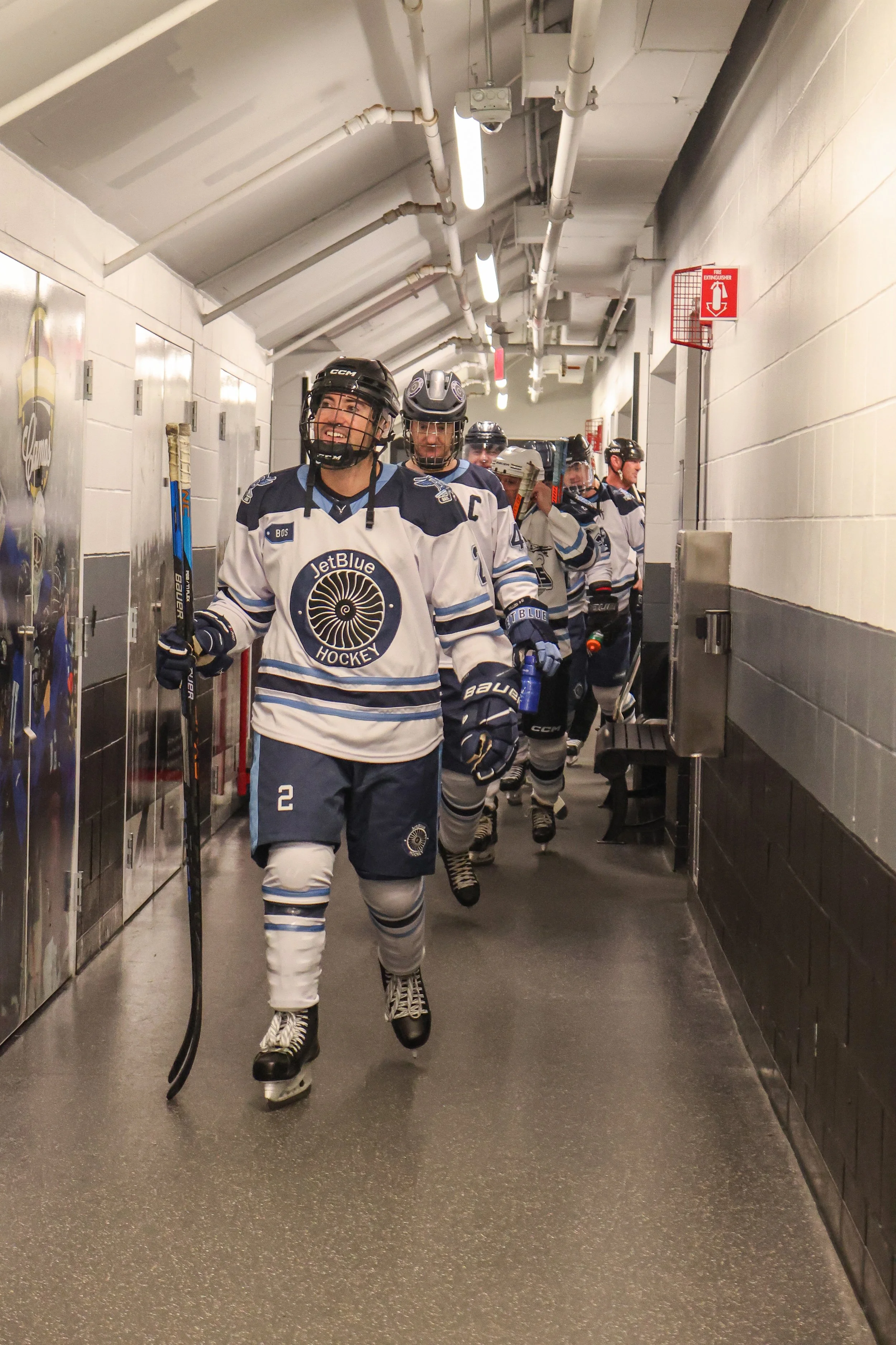 Hockey players in white and blue jerseys walking down a tunnel.
