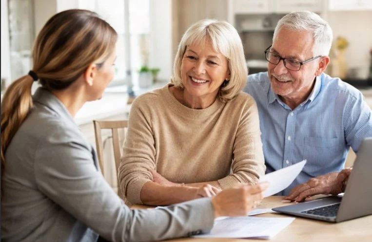 An older couple sitting with a young woman at a table, discussing documents with a laptop open.
