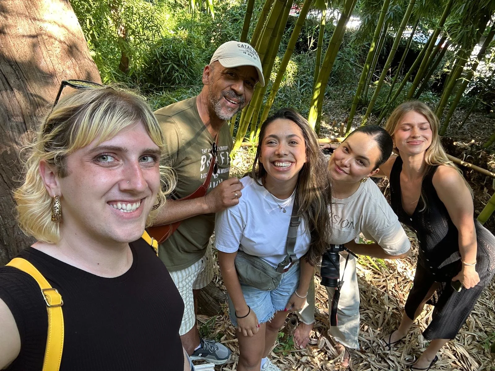 Group of five people smiling and posing in a lush outdoor setting with bamboo and leafy trees.