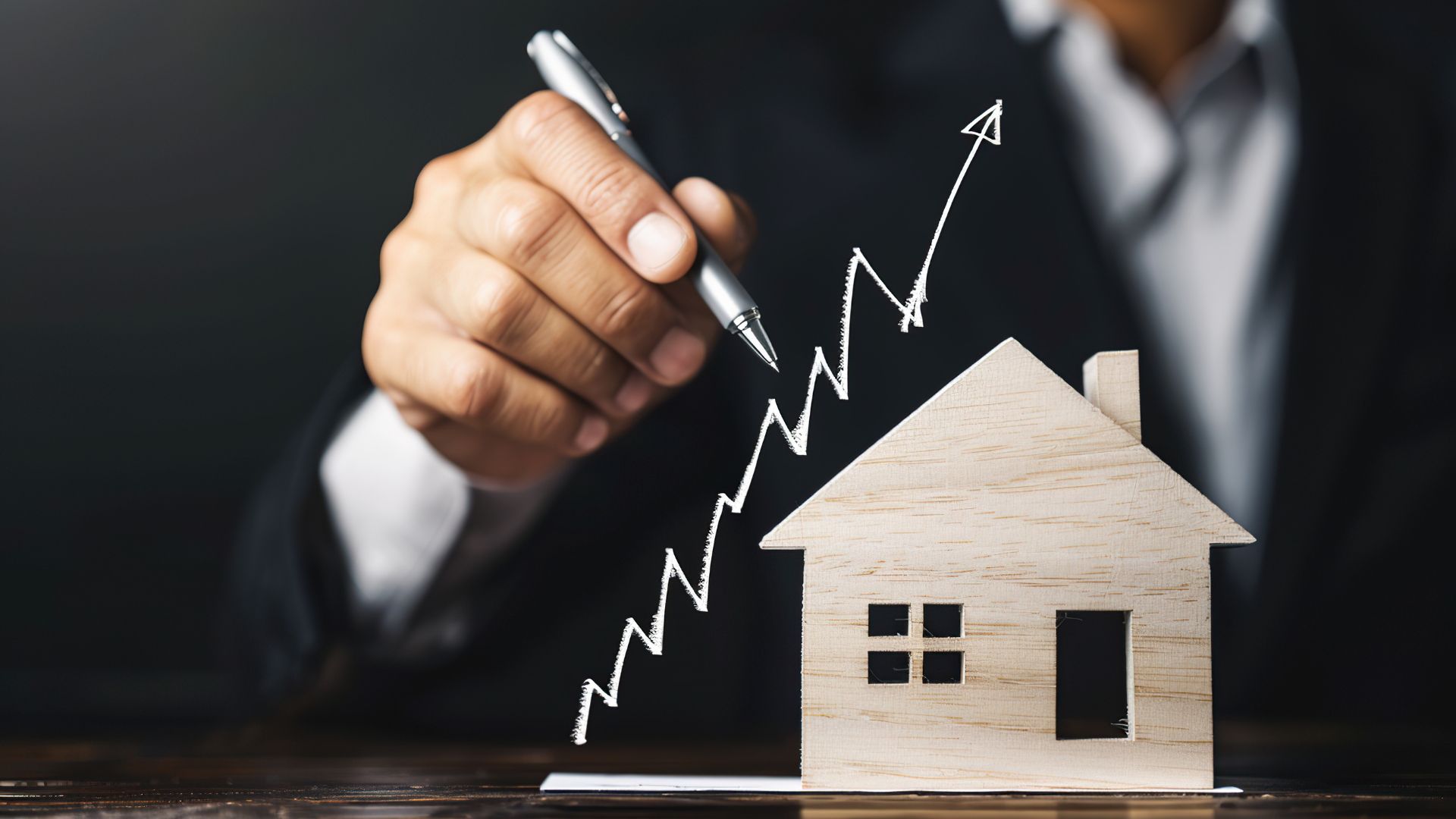 Man in suit drawing an upward trending graph on a blackboard next to a wooden house model.