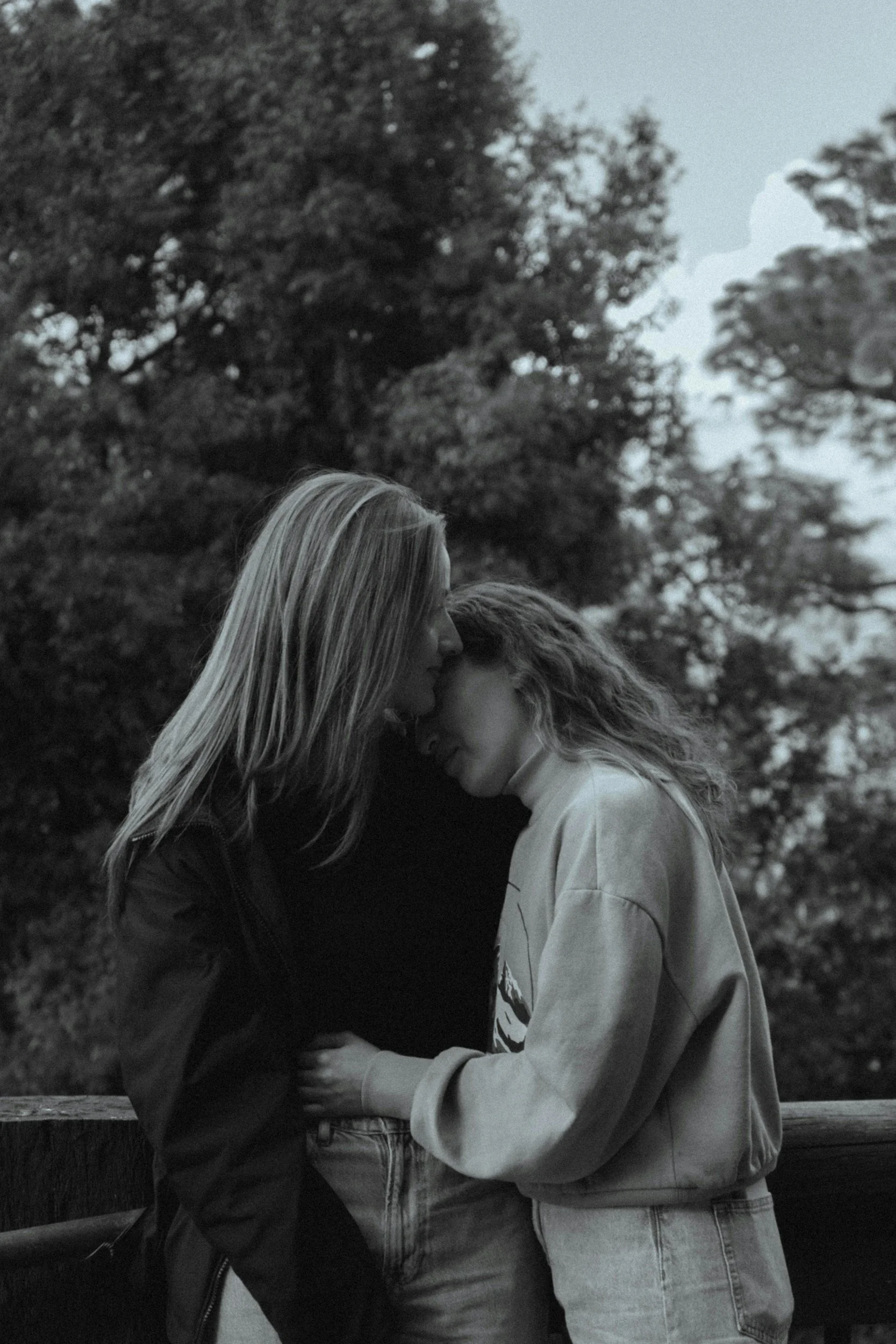 Black-and-white photograph of two women standing close together outdoors, sharing an affectionate moment.