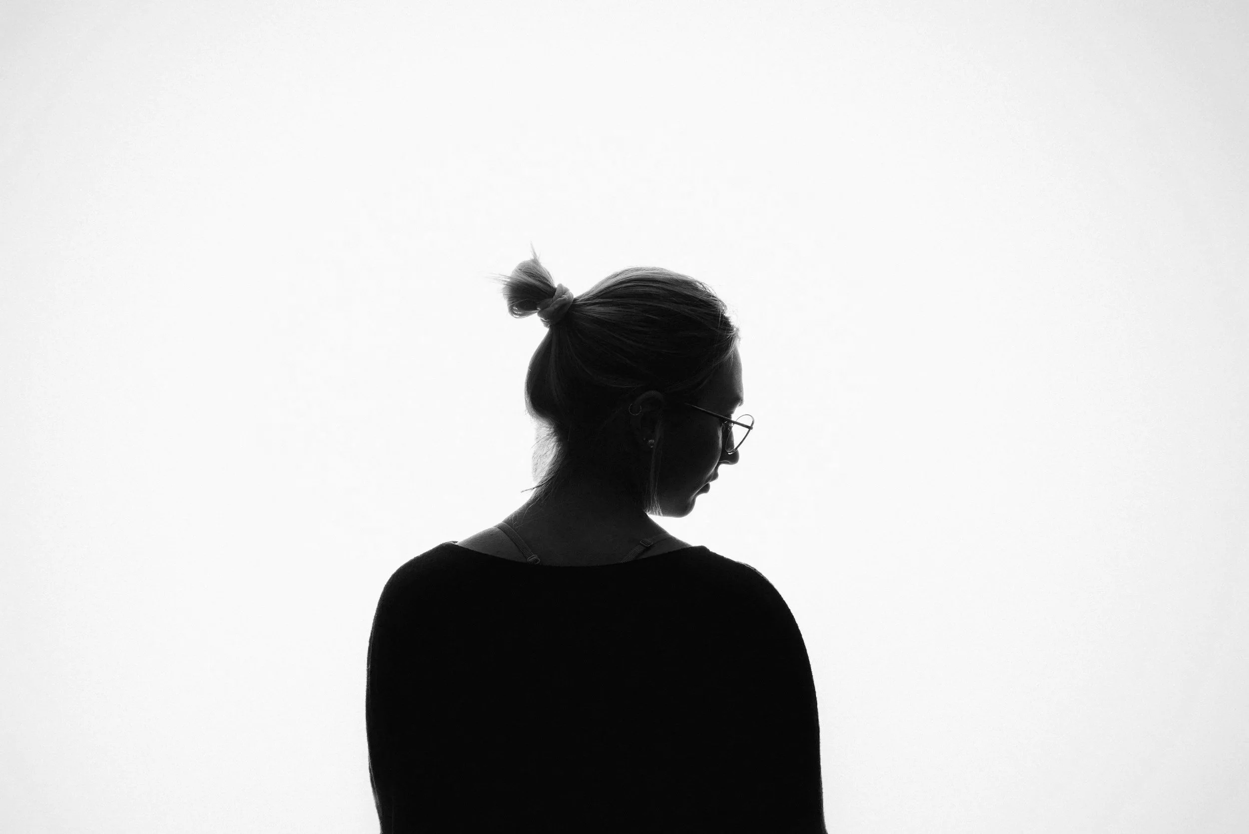 Black-and-white portrait of a woman with glasses and her hair tied up, looking down.