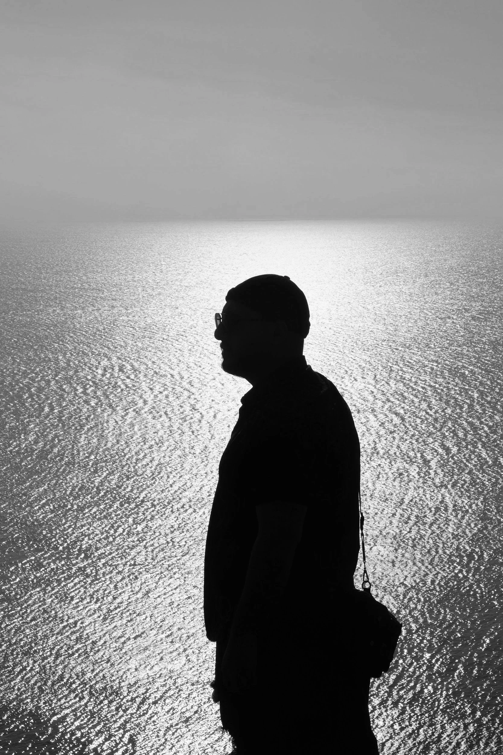 Silhouette of a man standing by the sea in a black-and-white photograph.