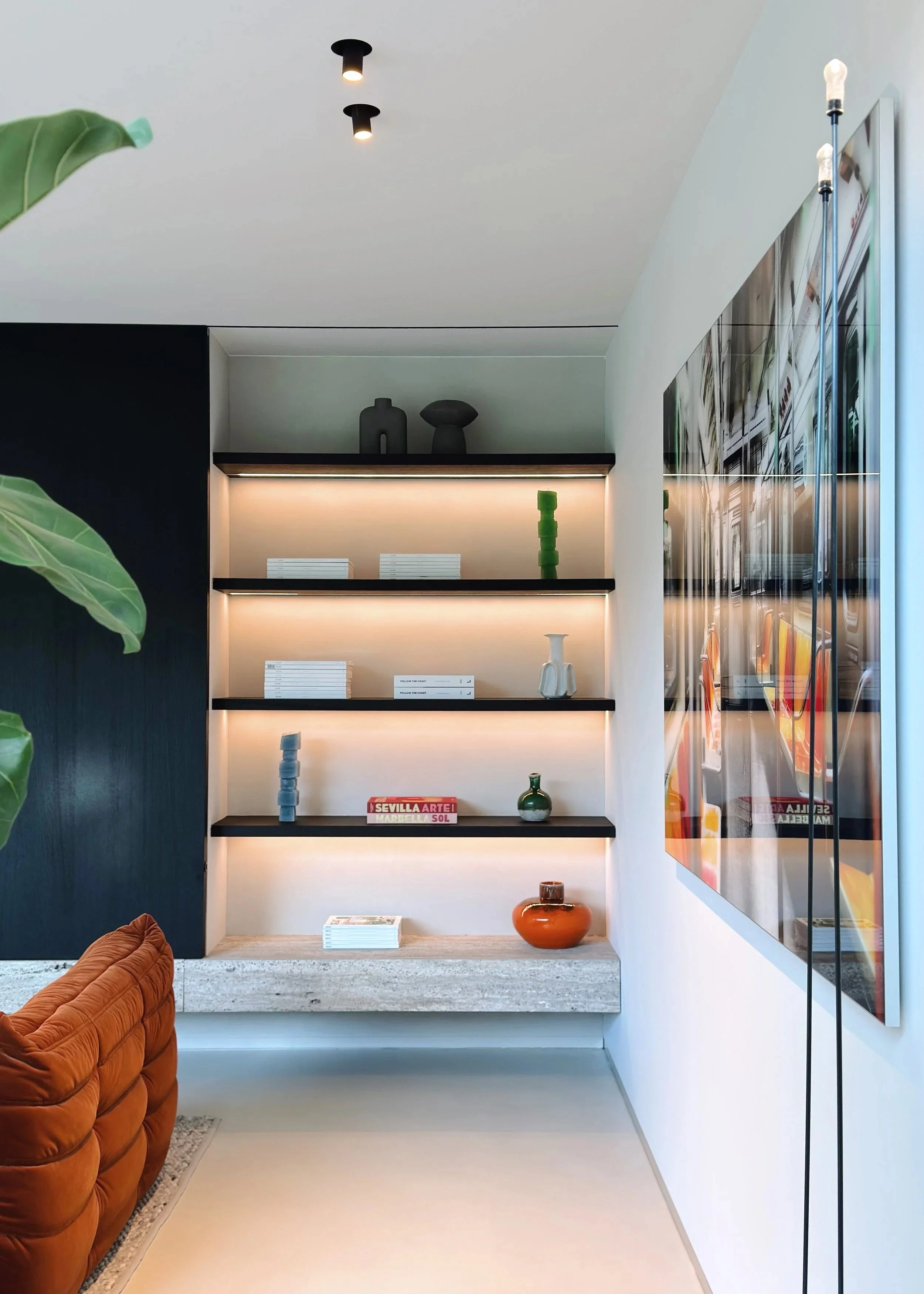 Une étagère murale décorative avec des objets en céramique, livres et un cadre de télévision mural dans un salon moderne.