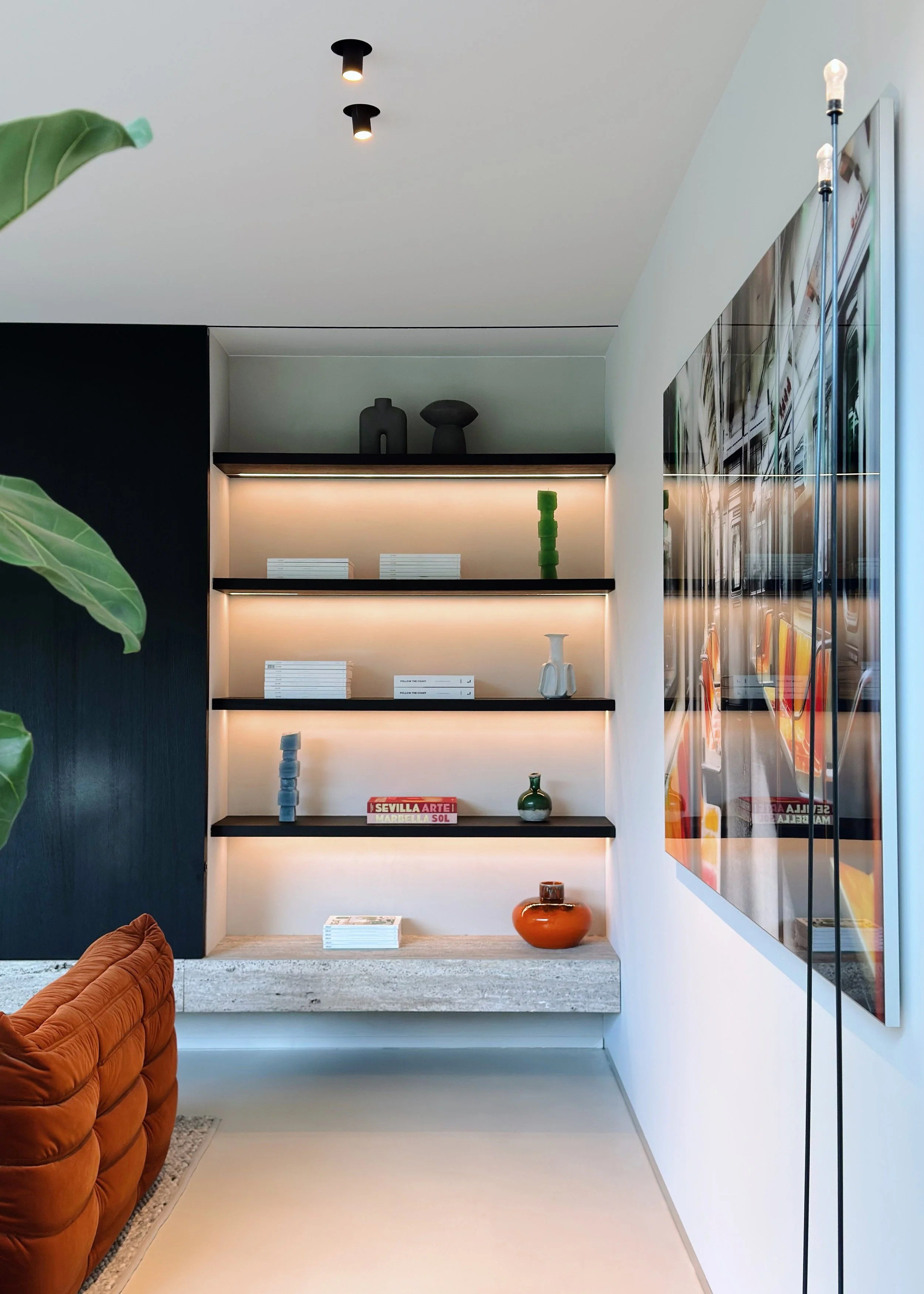 Intérieur moderne avec étagères éclairées contenant des décorations, un mur noir, un canapé orange et un mur blanc avec une grande fenêtre.