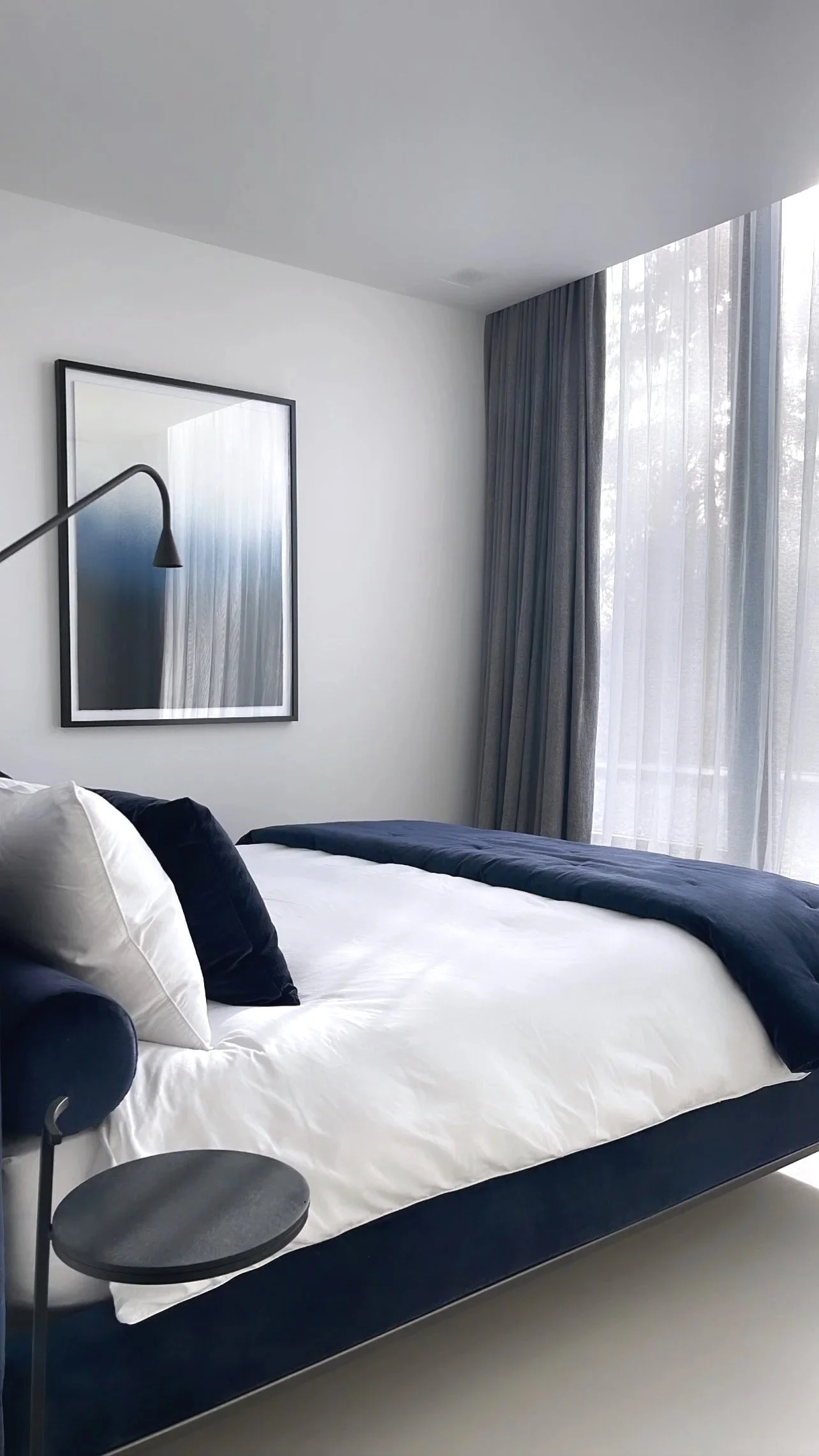 Chambre moderne avec lit blanc, rideaux bleus et miroir au mur.