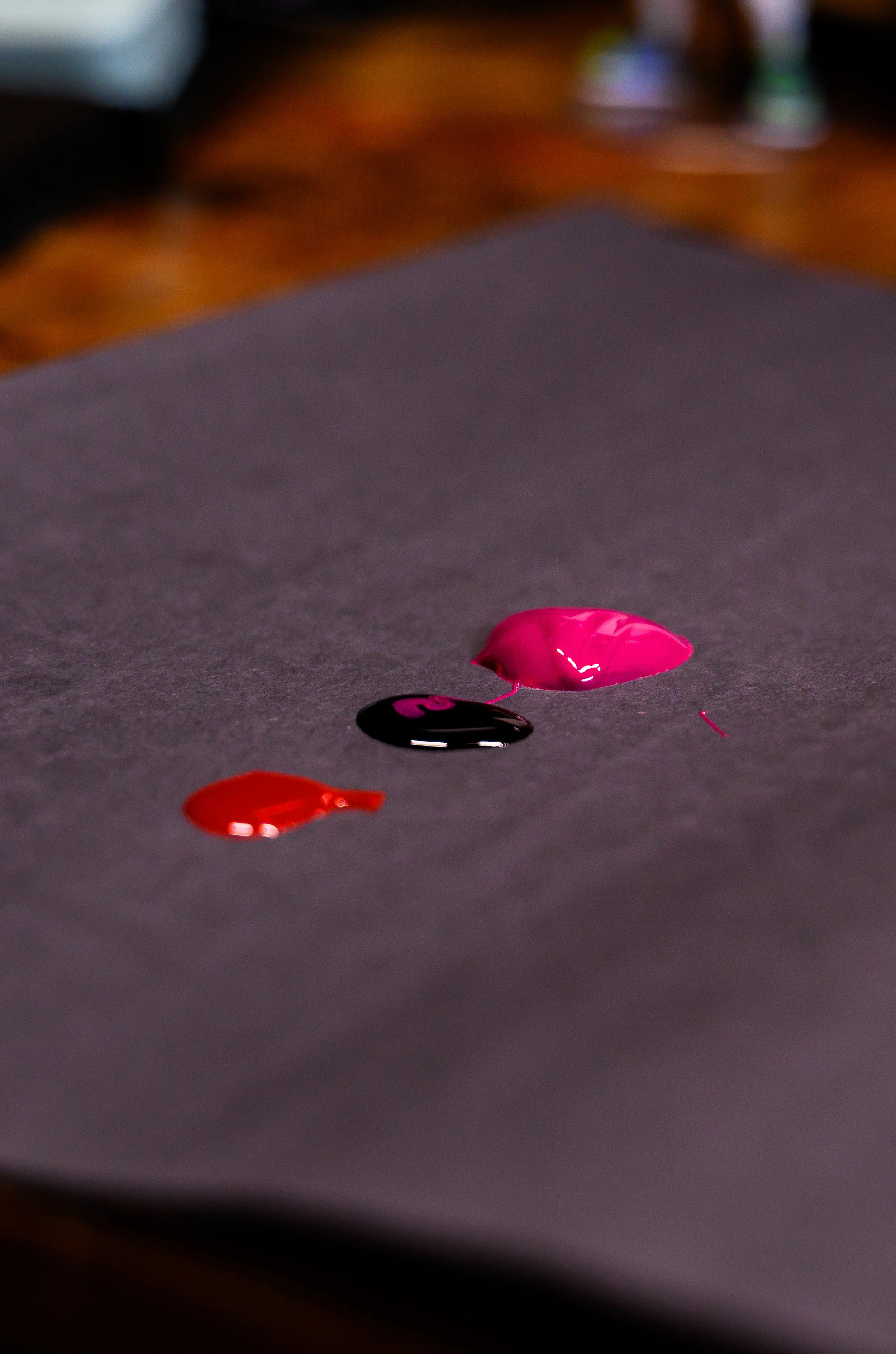Close-up of dollop of red, black, and pink paint on dark gray surface.
