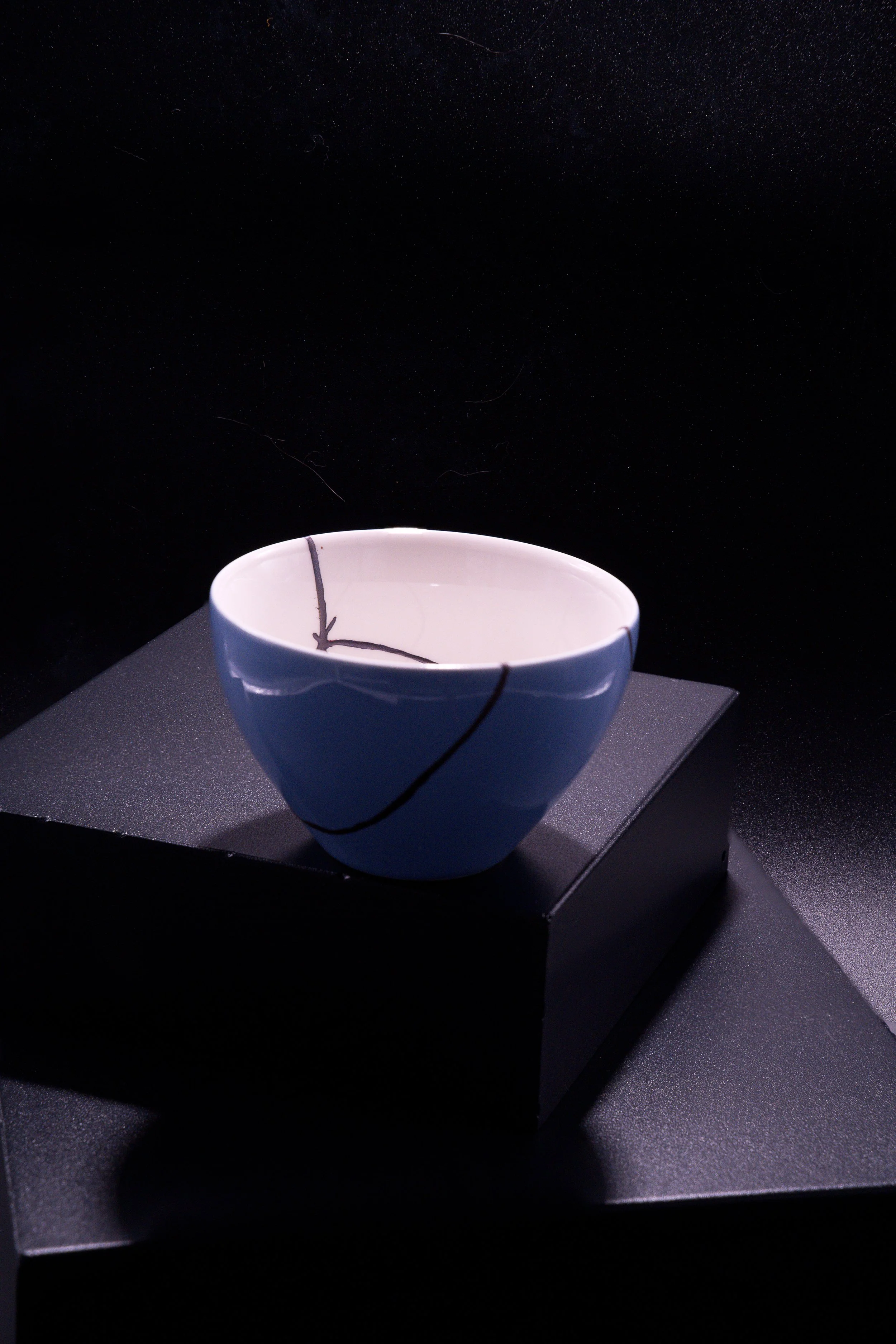 A white ceramic bowl with black lines, on a black pedestal, against a dark background.
