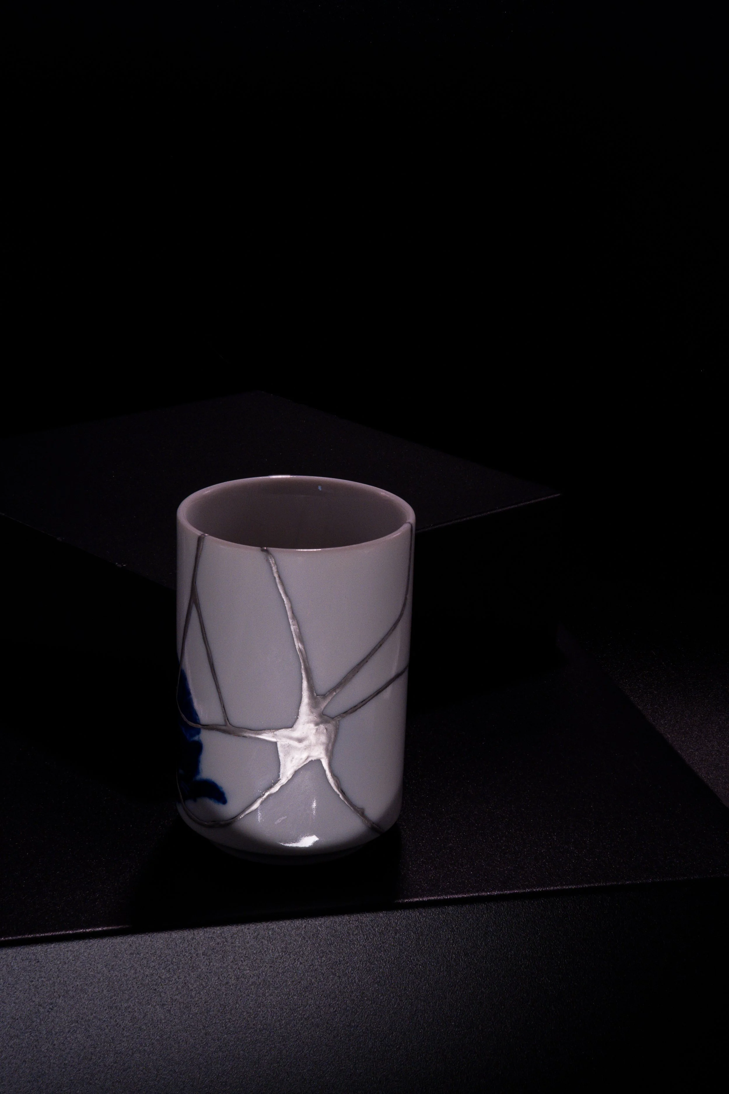 A white ceramic mug with a crackled glaze design, placed on a black surface against a black background.