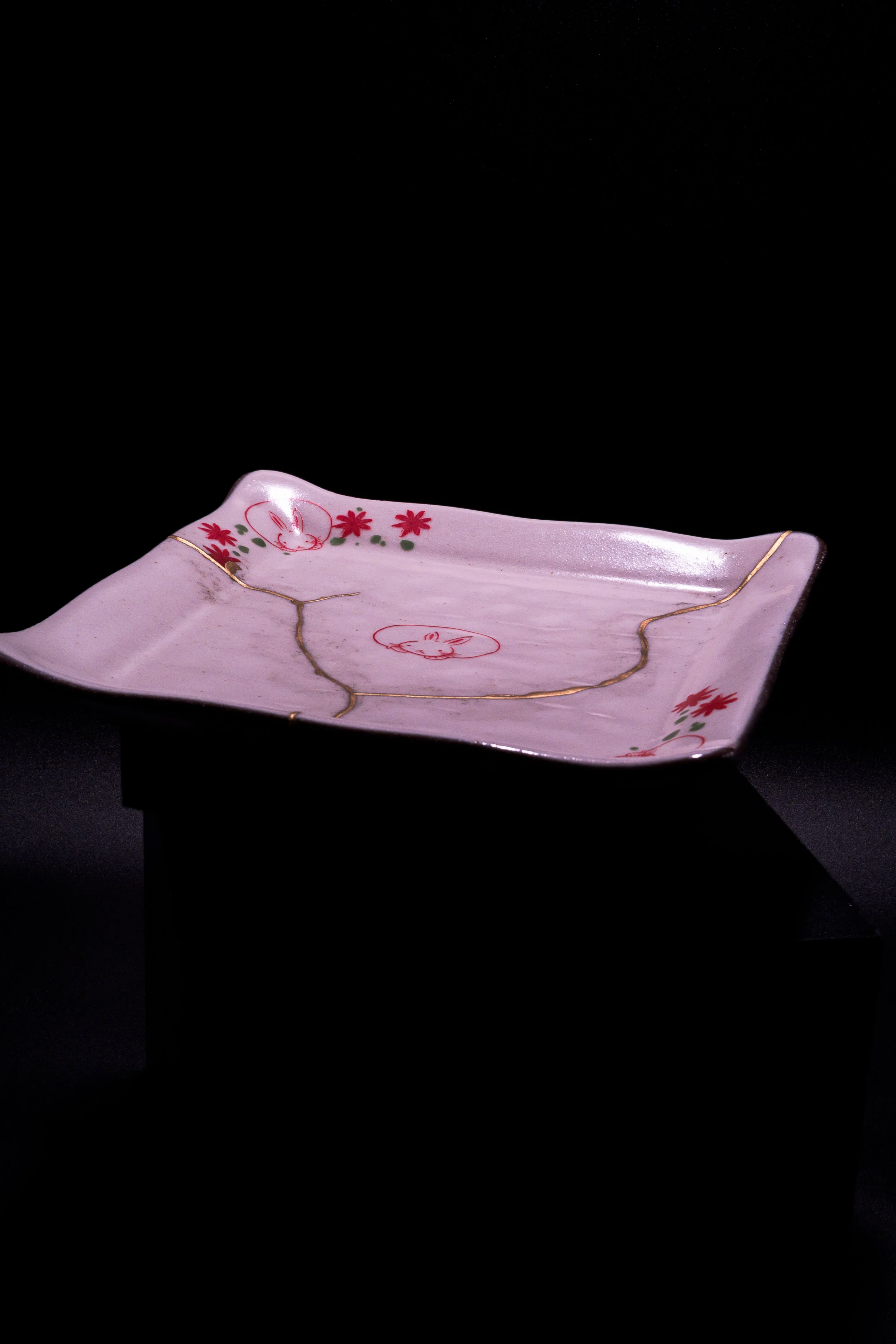 Decorative pink ceramic plate with red flower designs and gold accents on a black background.