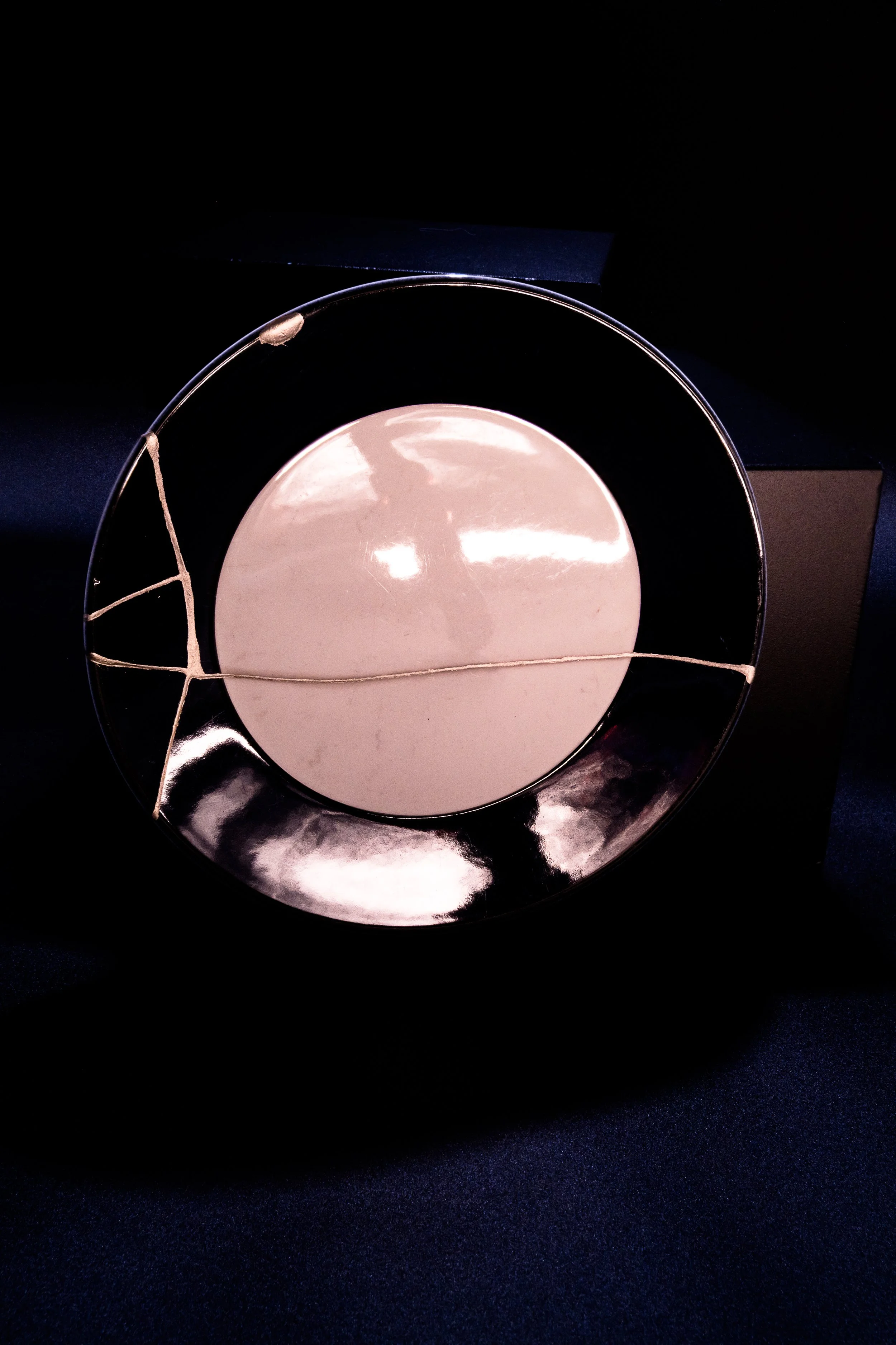 A round mirror with a reflective glass surface, framed by a black circle. The mirror has a thin string stretched across it, divided into three sections. The background appears to be a dark fabric.