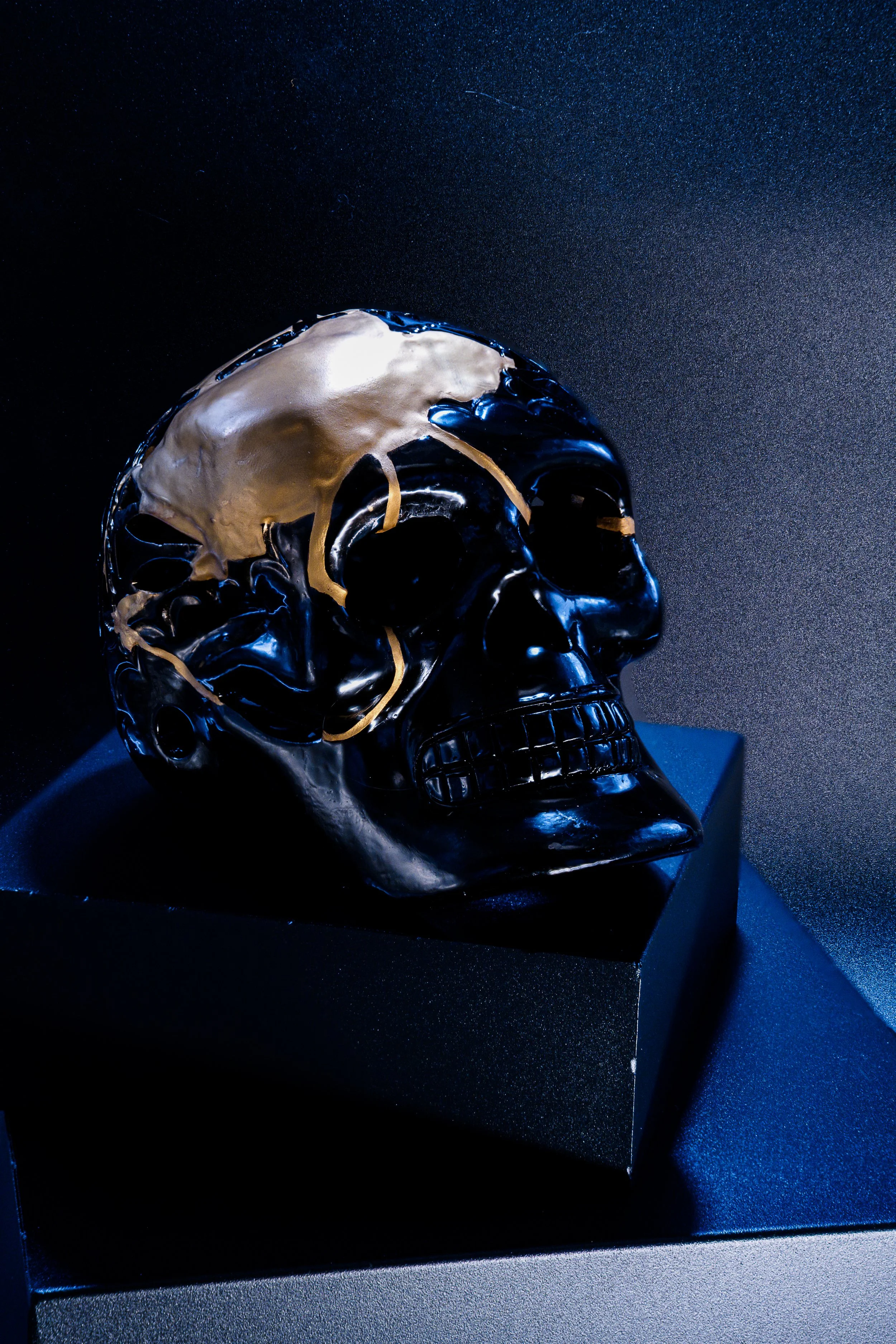 Black skull sculpture with gold accents on display in a dark room.