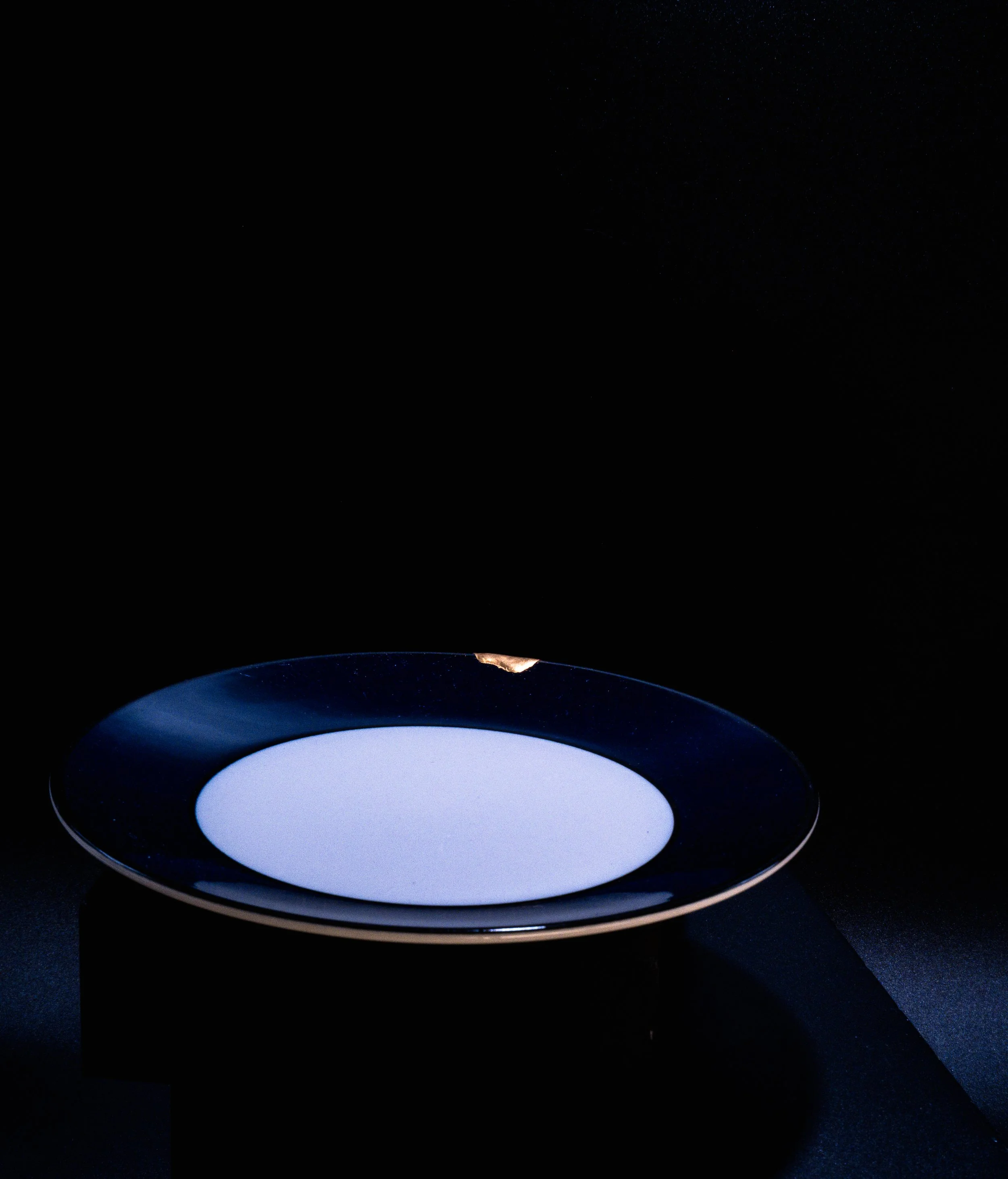 A circular white light panel on a black pedestal, set against a black background.