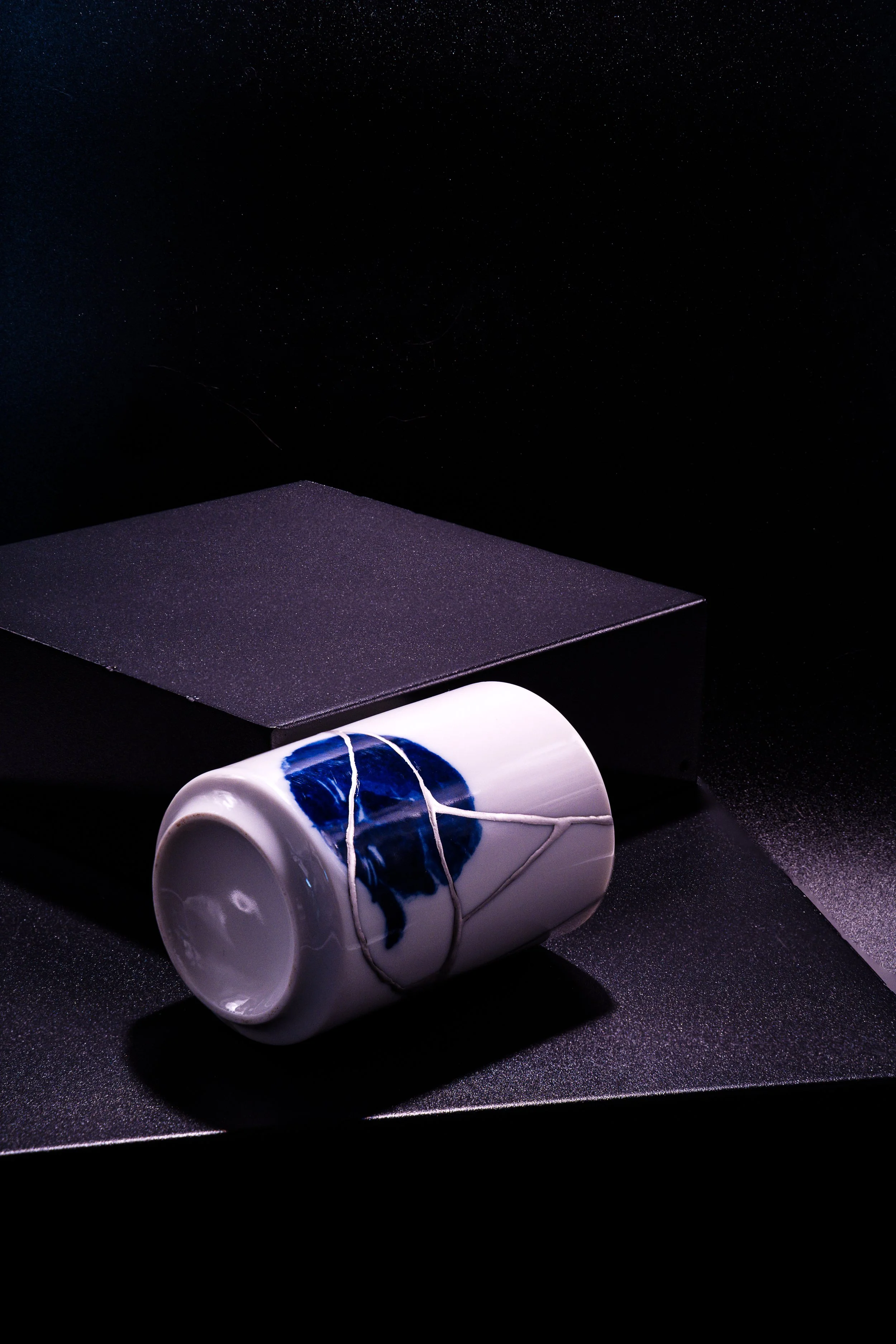 A white cup with blue design, wrapped with white string, placed on a black platform against a dark background with a starry sky.