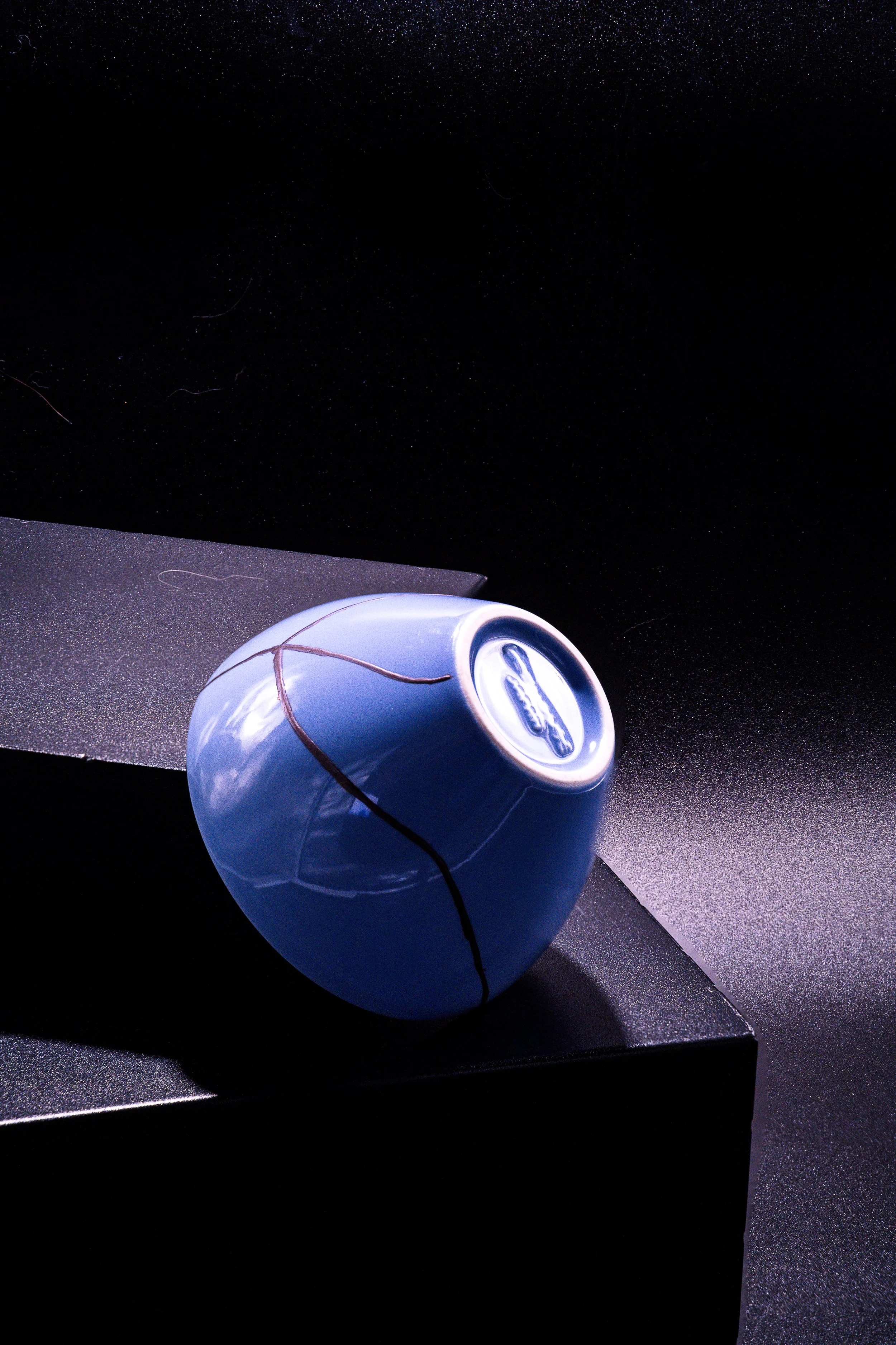 A blue soda can placed in a cracked, jagged ceramic or stone vessel on a dark surface with a dark background.