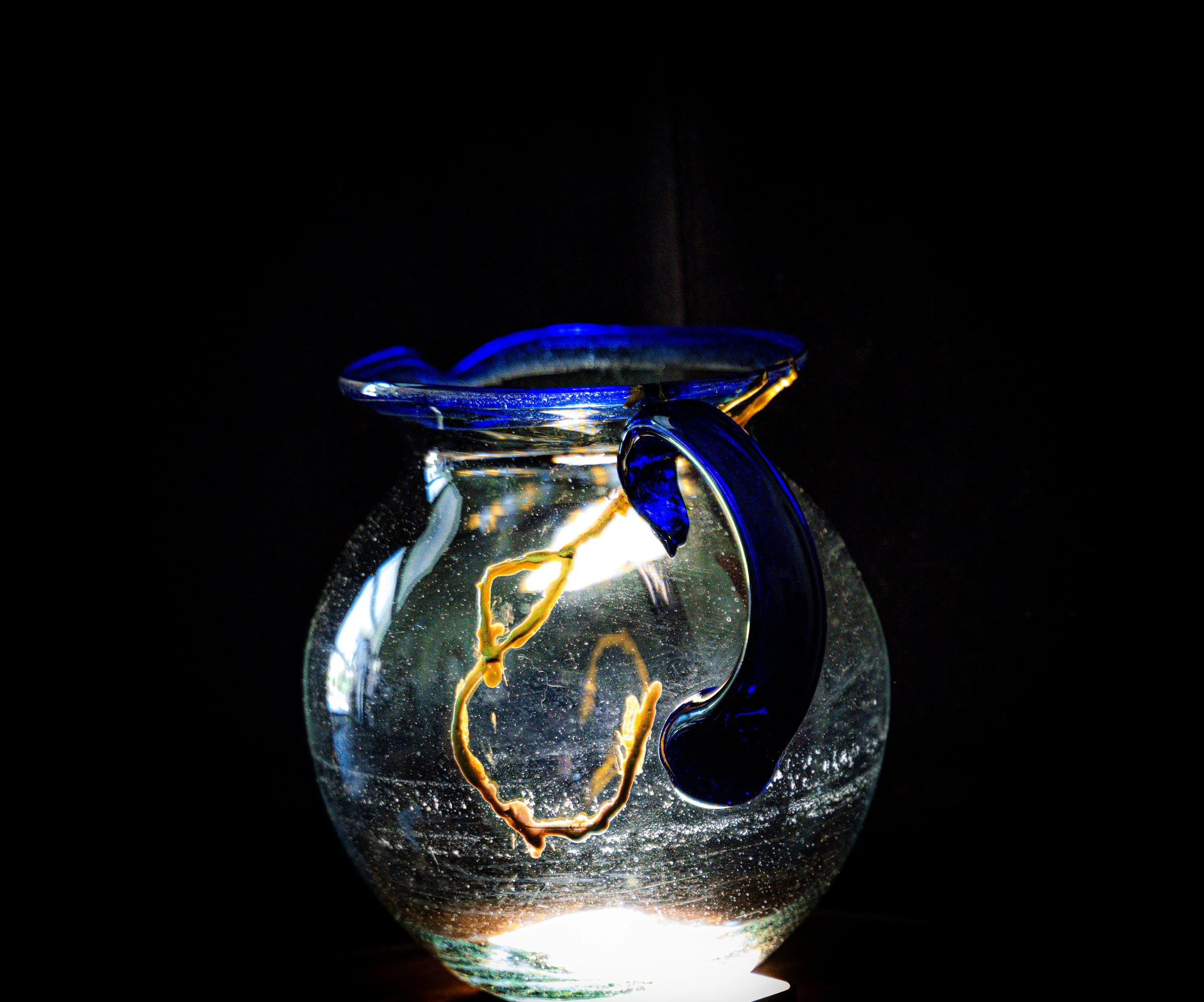 Glass plunger with swirling colored liquid, illuminated against a black background.