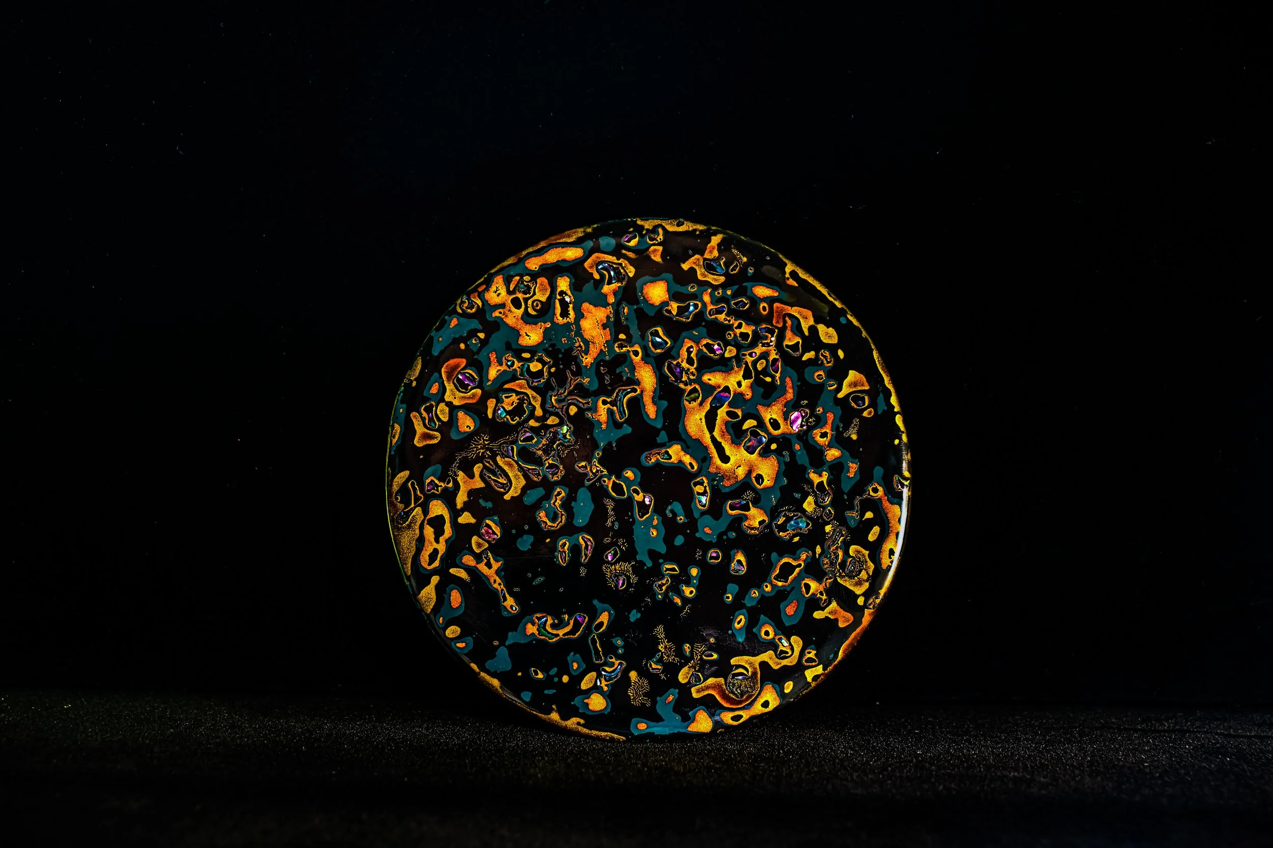 A glass art piece with swirling colorful patterns illuminated against a black background.