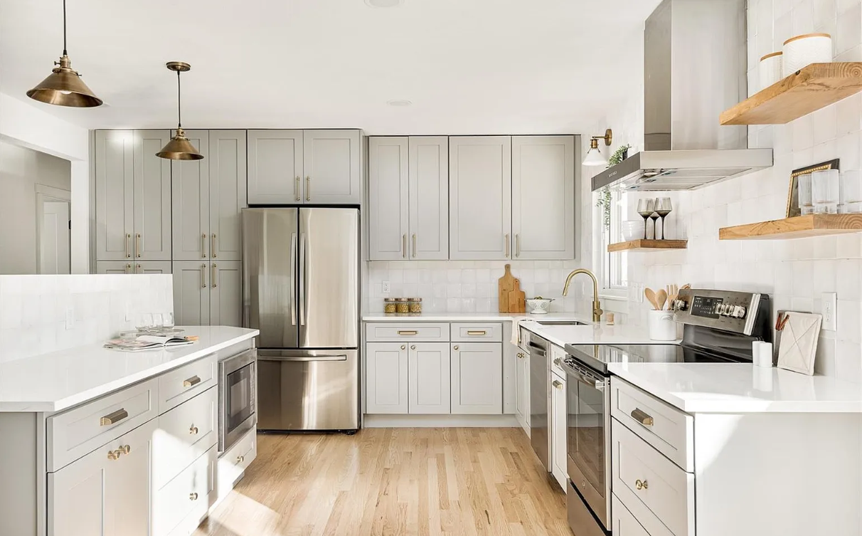 Modern kitchen with white cabinets, stainless steel refrigerator, microwave, and stove, wooden floating shelves, and light hardwood floors.